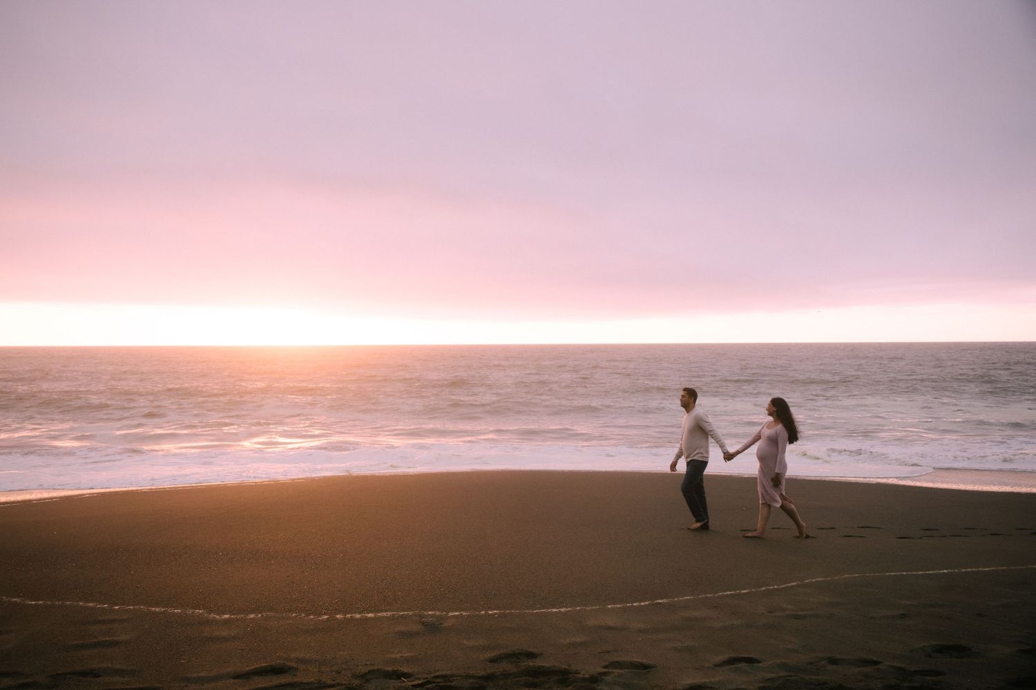Distant figures walking along empty beach at sunset with dramatic sky.