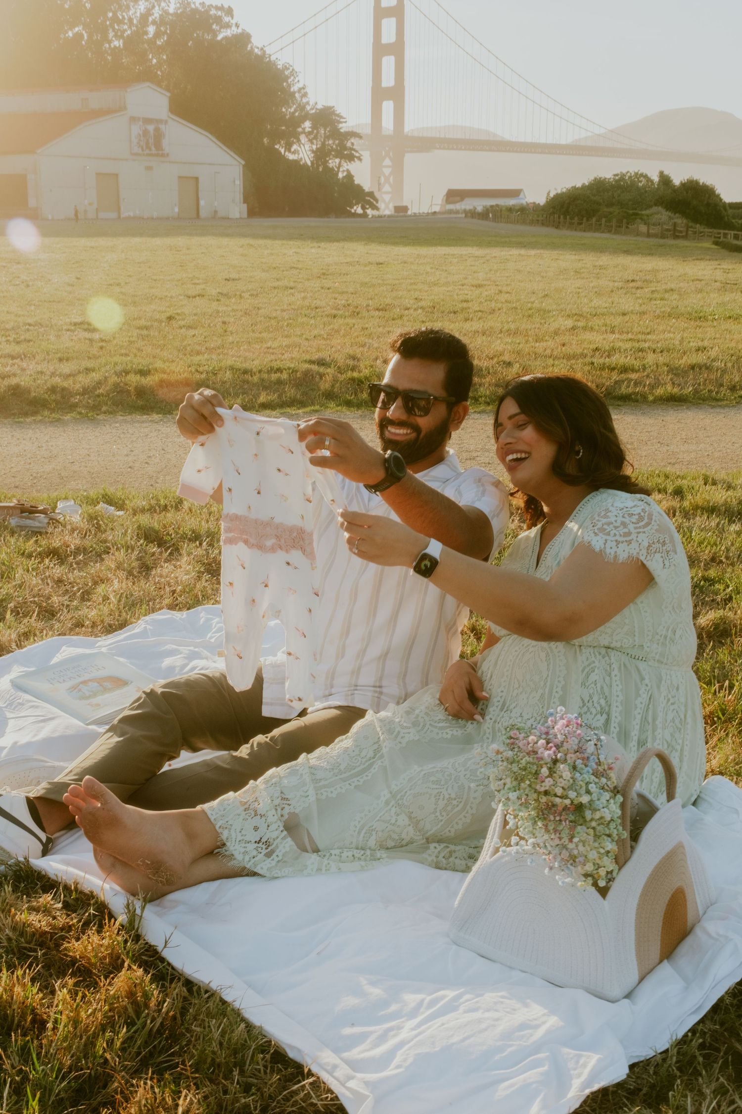 Couple relaxing on picnic blanket near Golden Gate Bridge at sunset.