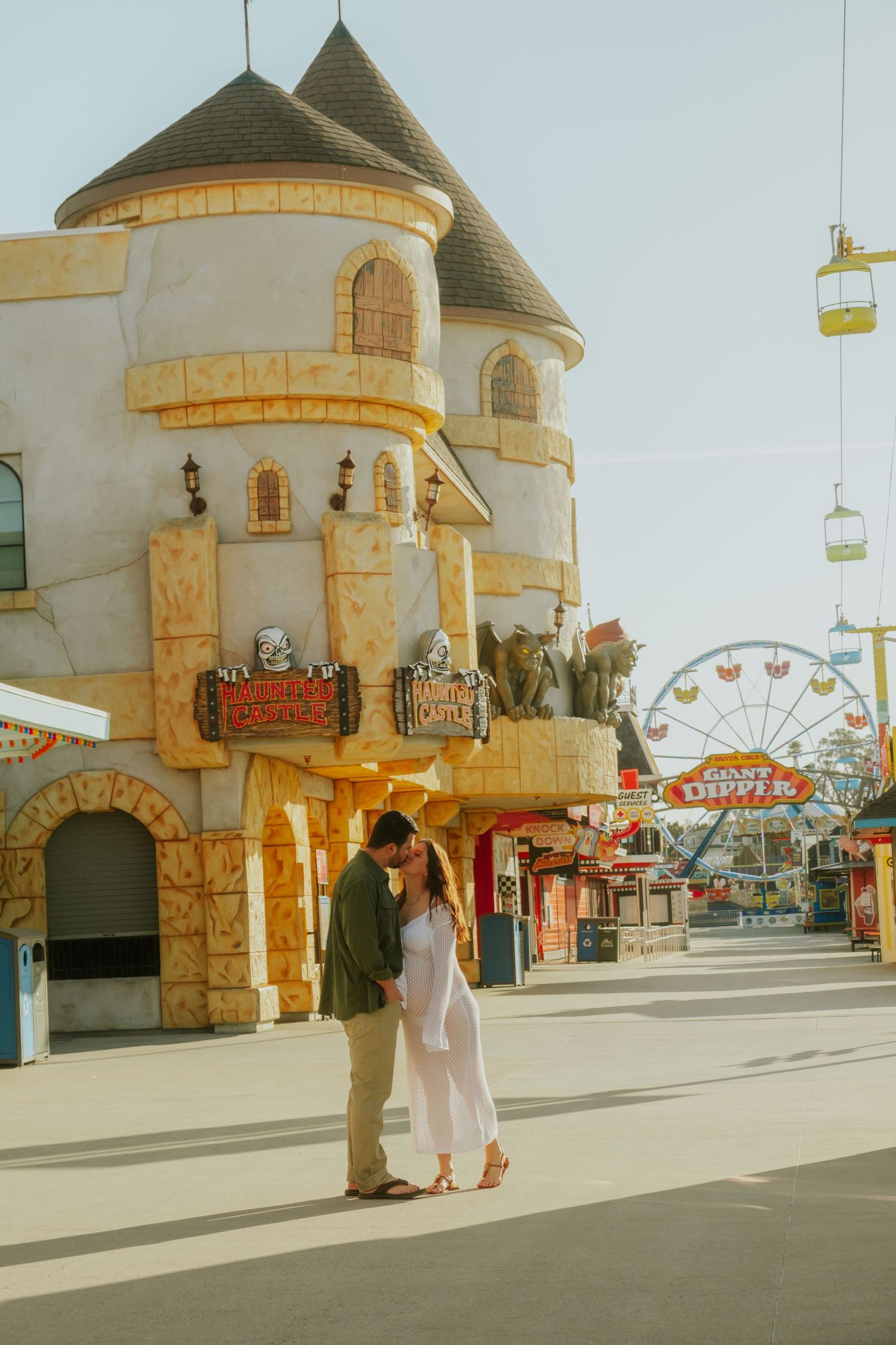 A couple poses in front of castle-like architecture at a boardwalk amusement park.