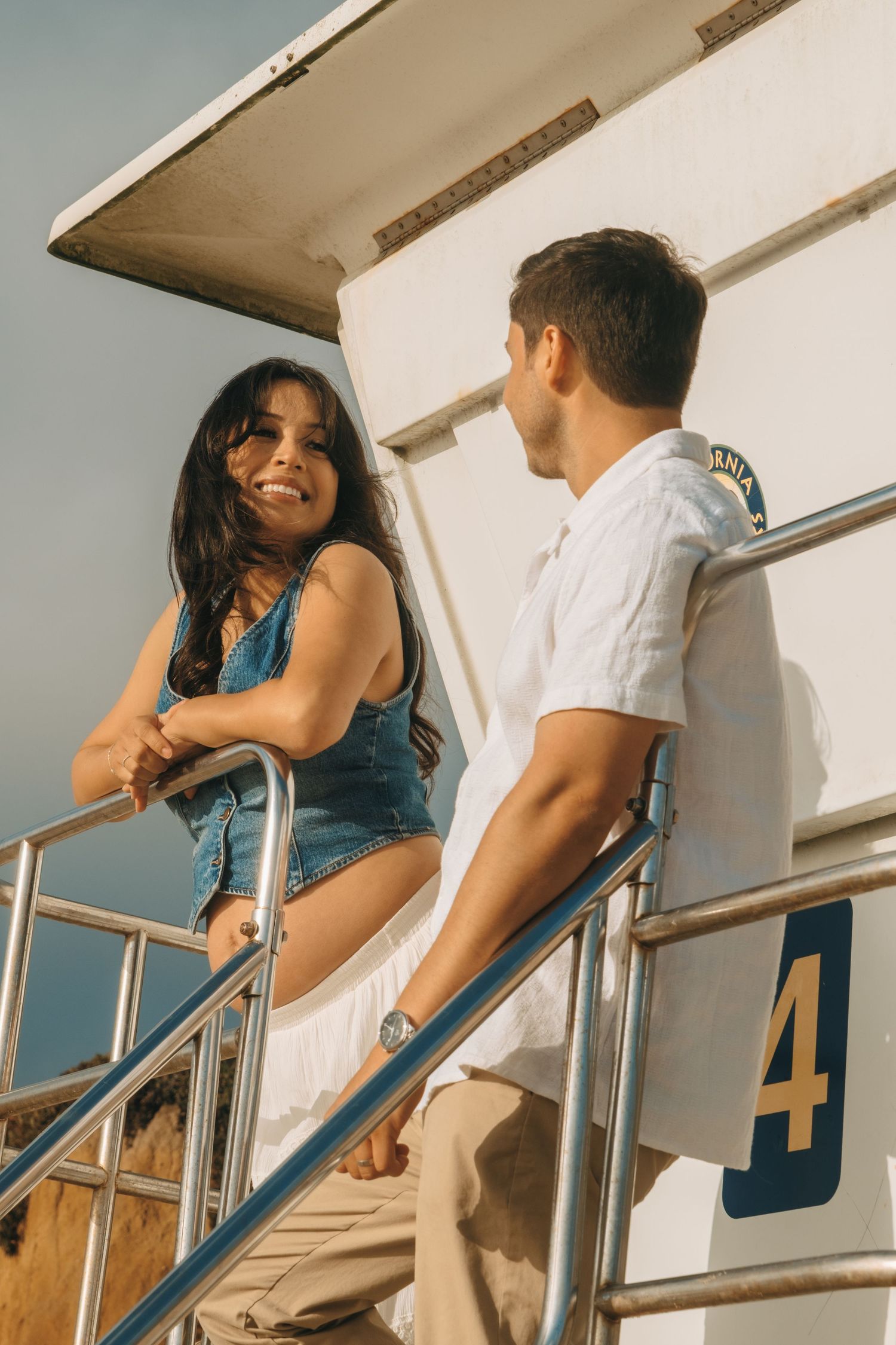 A couple shares romantic moments on a white lifeguard tower at the beach.