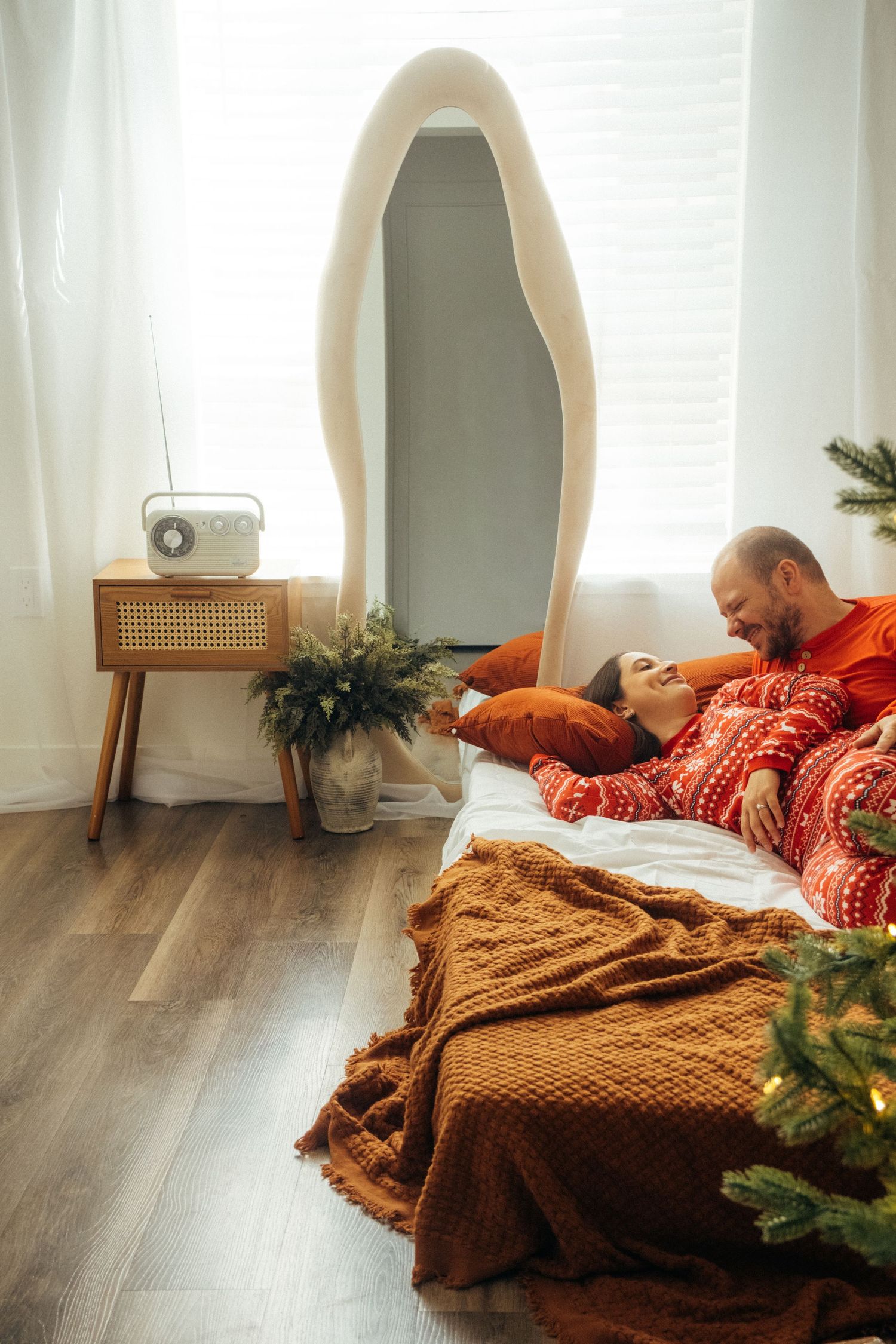 Modern holiday bedroom setup with oval mirror, wooden side table and cozy knit blankets.