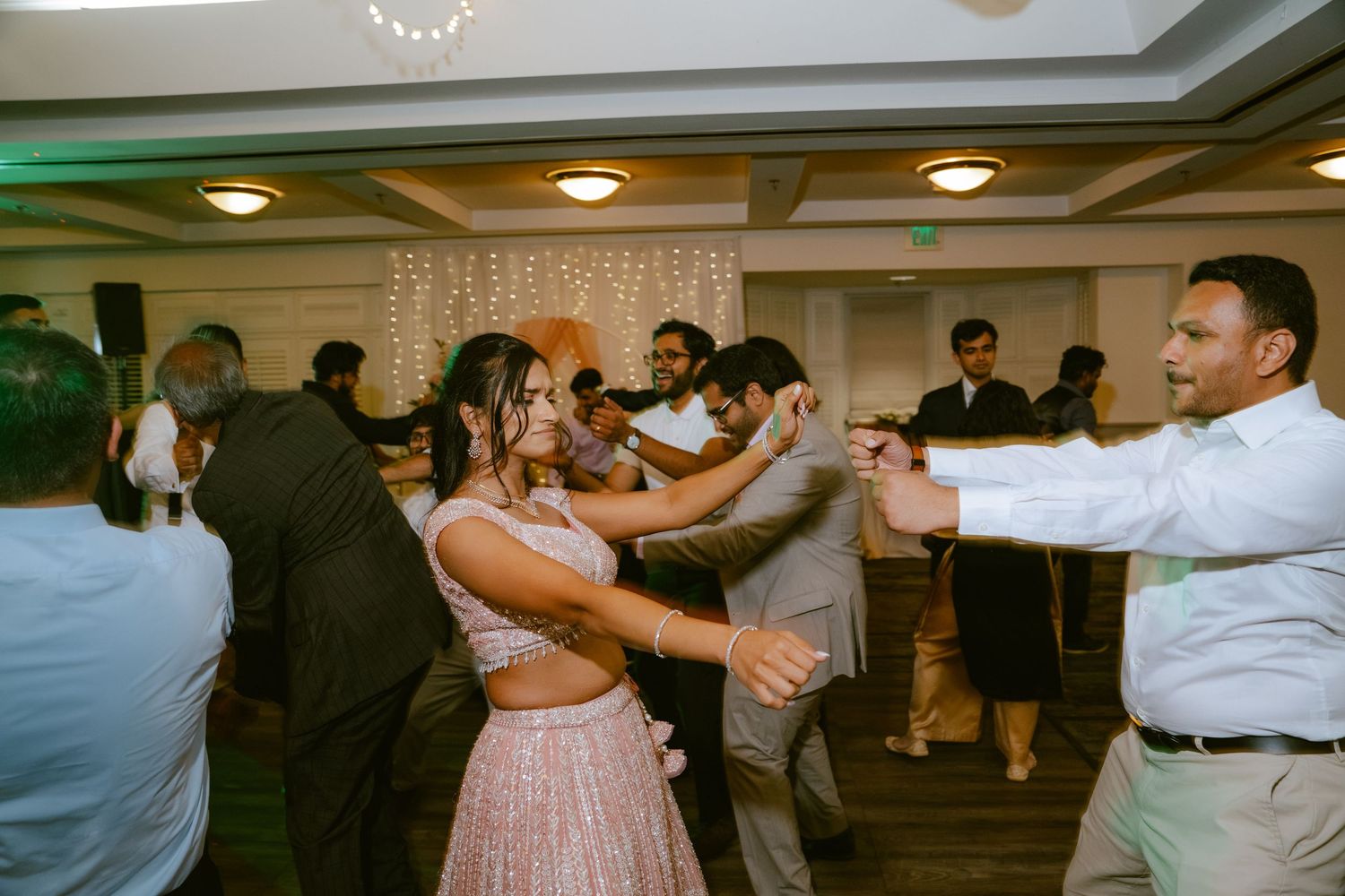 Guests dancing joyfully at an indoor wedding reception with fairy lights and elegant decor.