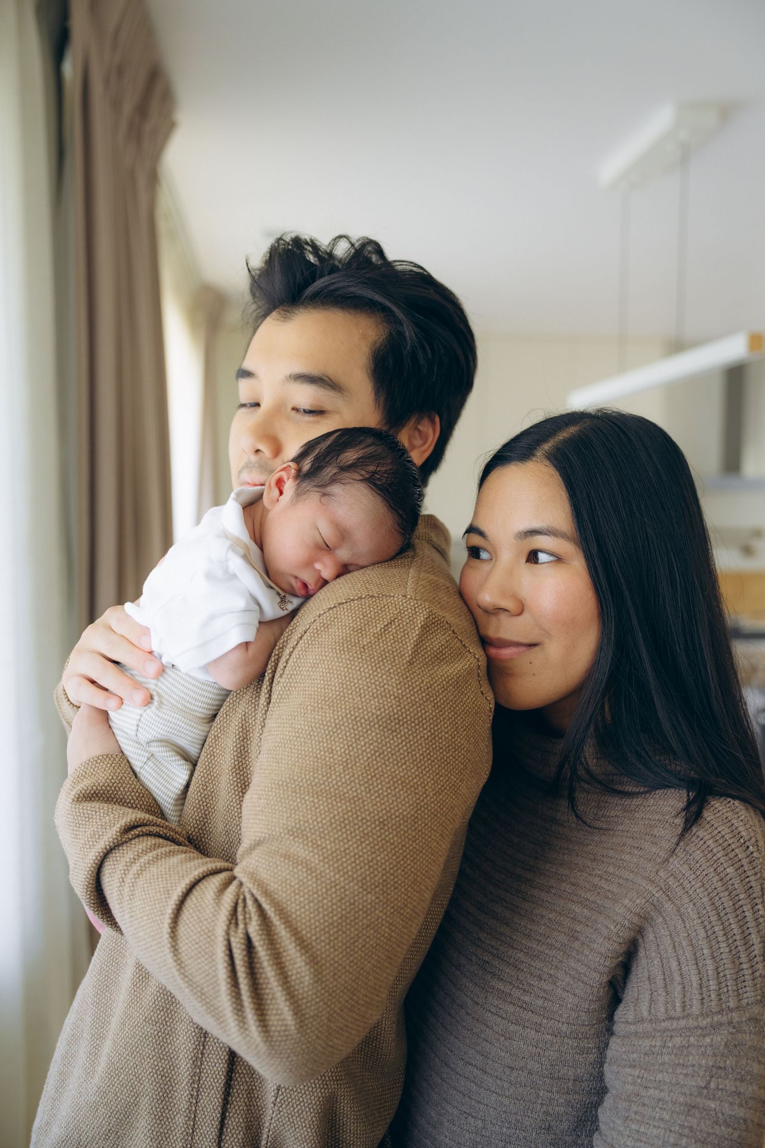 Asian parents tenderly holding their sleeping newborn baby at home, sharing a loving family moment.