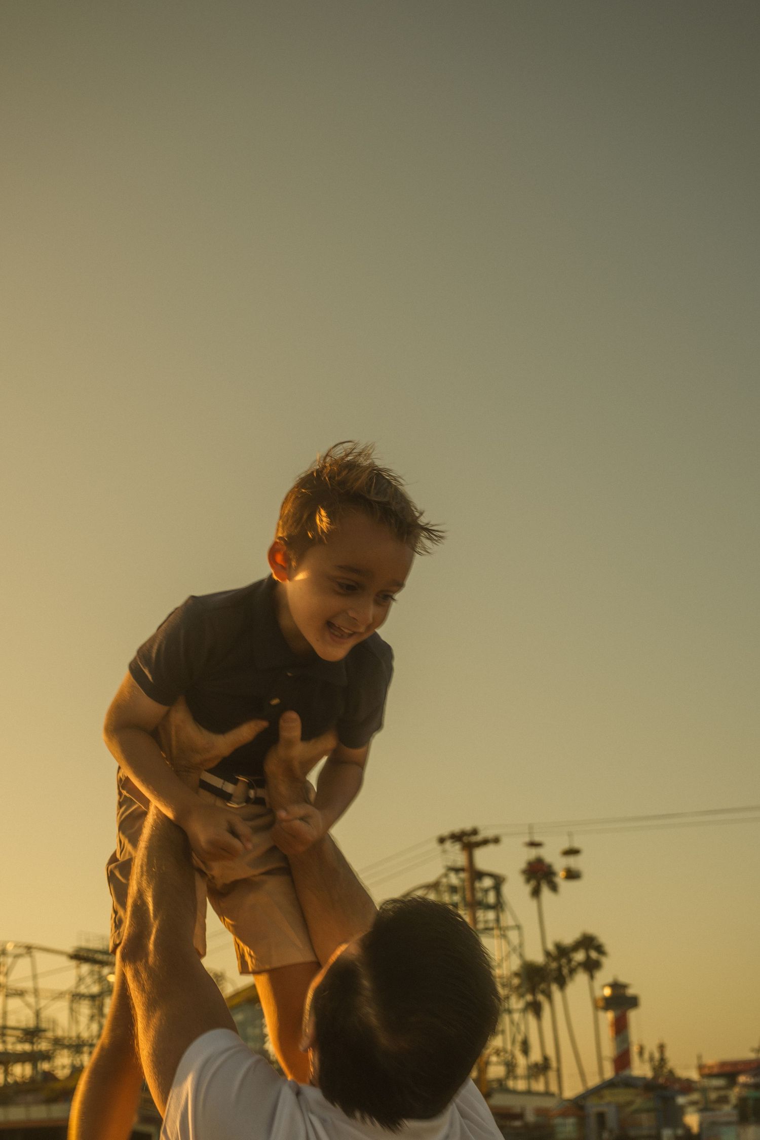 A joyful parent lifting child into the air at sunset with palm trees in background.