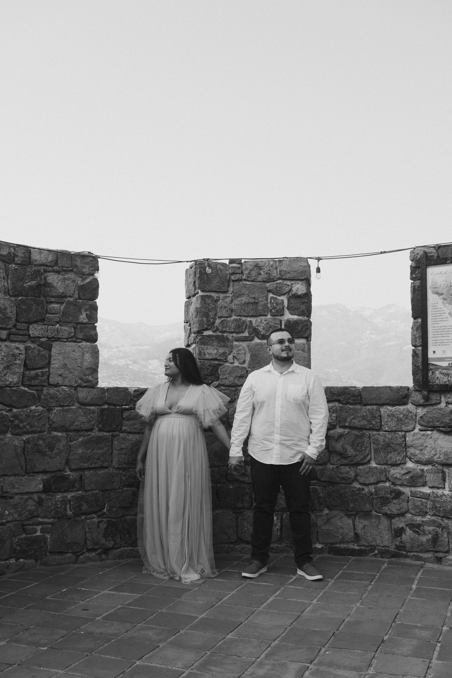 A romantic photoshoot in front of an ancient stone castle wall with dramatic lighting and shadows.