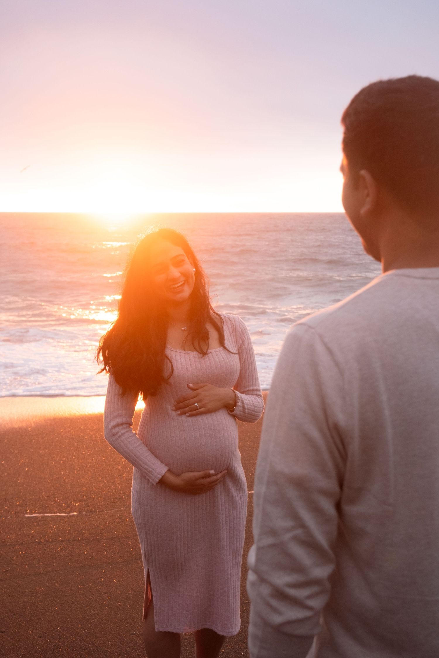 Silhouettes of a couple standing together on a beach at sunset with ocean waves in the background.