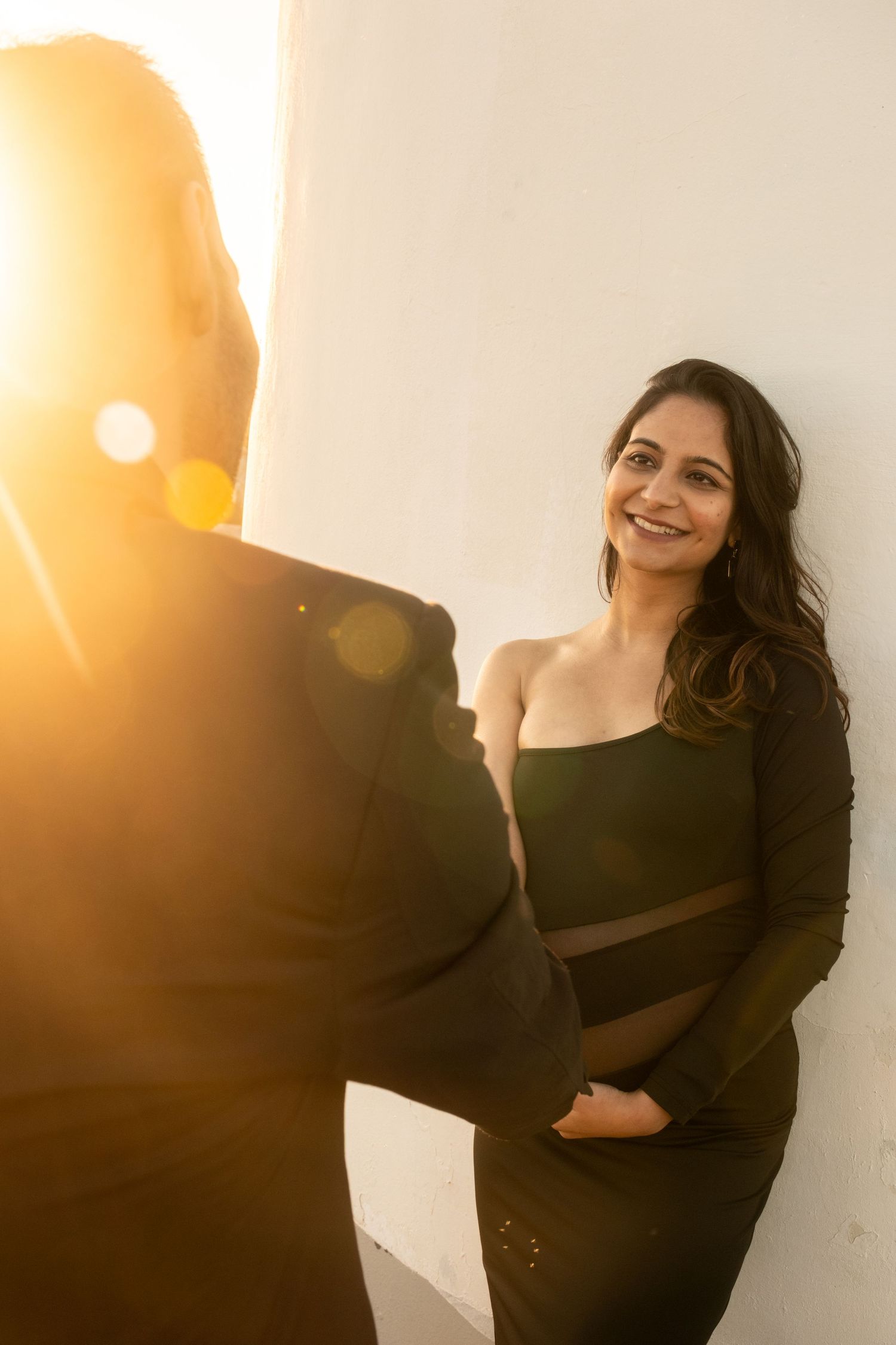 Maternity photoshoot with dramatic sunlight and white wall backdrop.