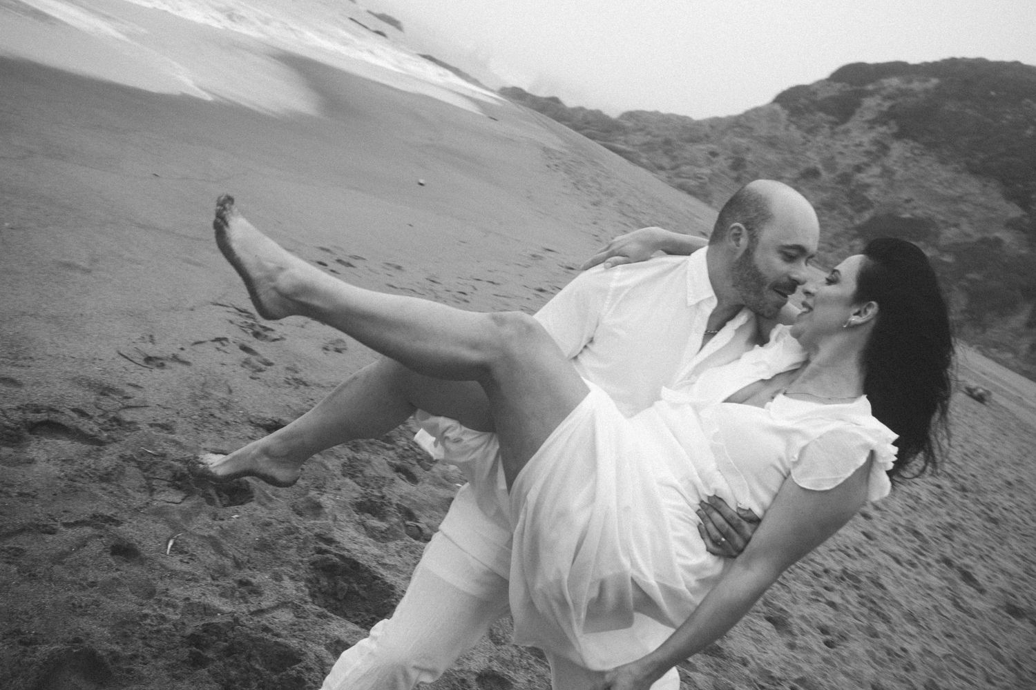 Couple playing and dancing together on a sandy beach during sunset.