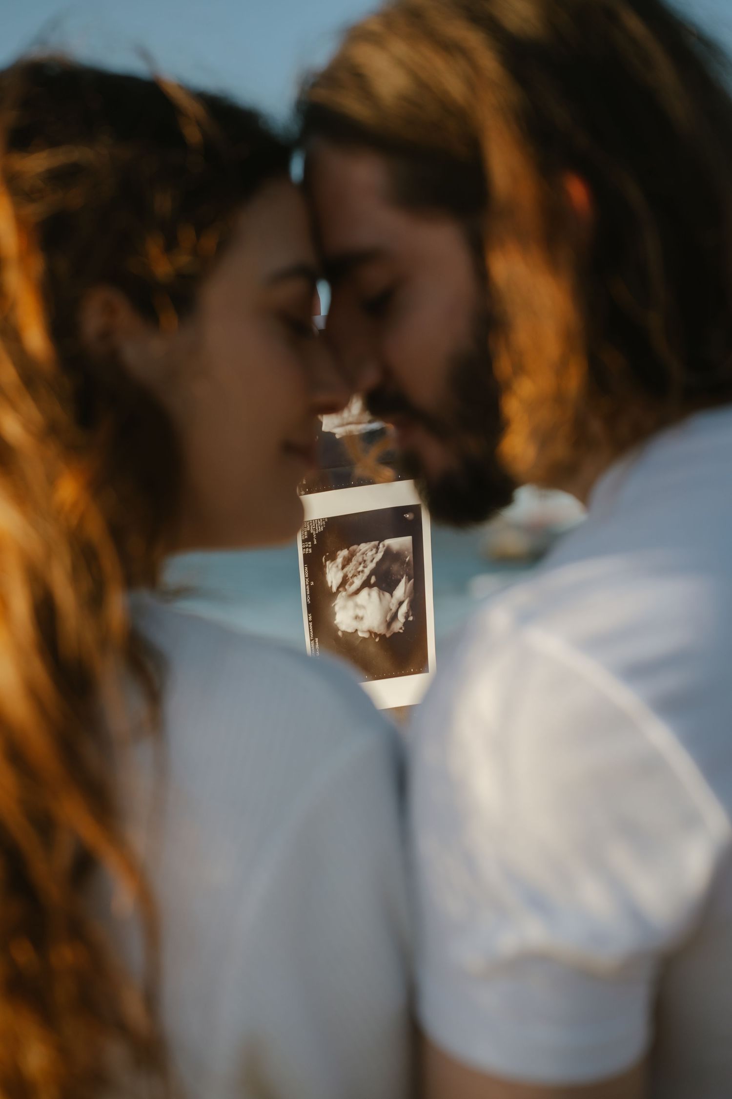 Couple in white shirts holding ultrasound photo, sharing a tender moment, pregnancy announcement portrait.