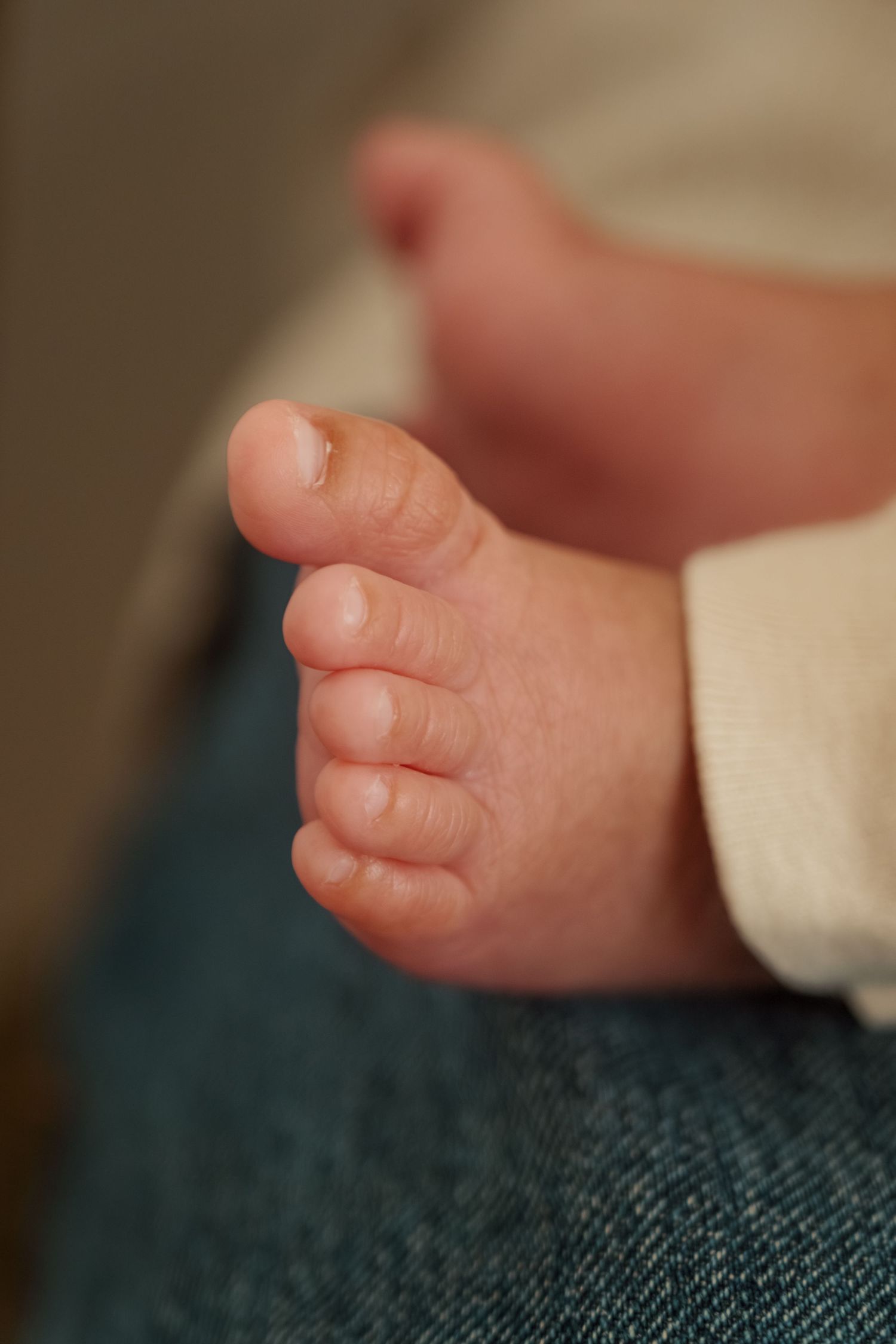 Close-up of tiny baby toes resting on dark denim fabric.