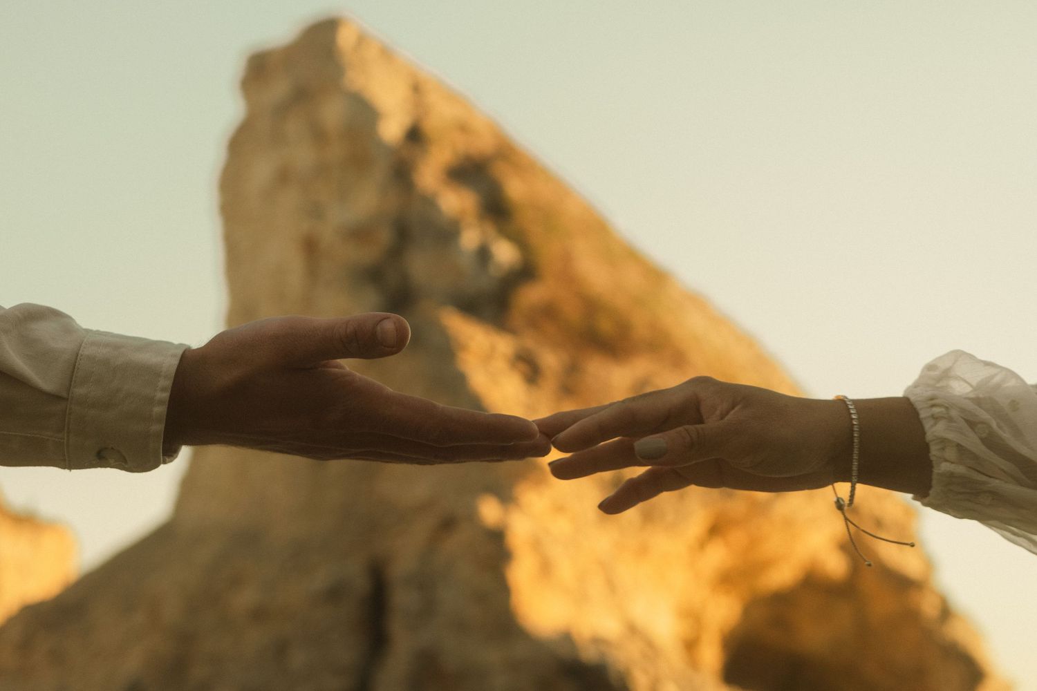 Reaching hands silhouetted against golden coastal cliffs at sunset.