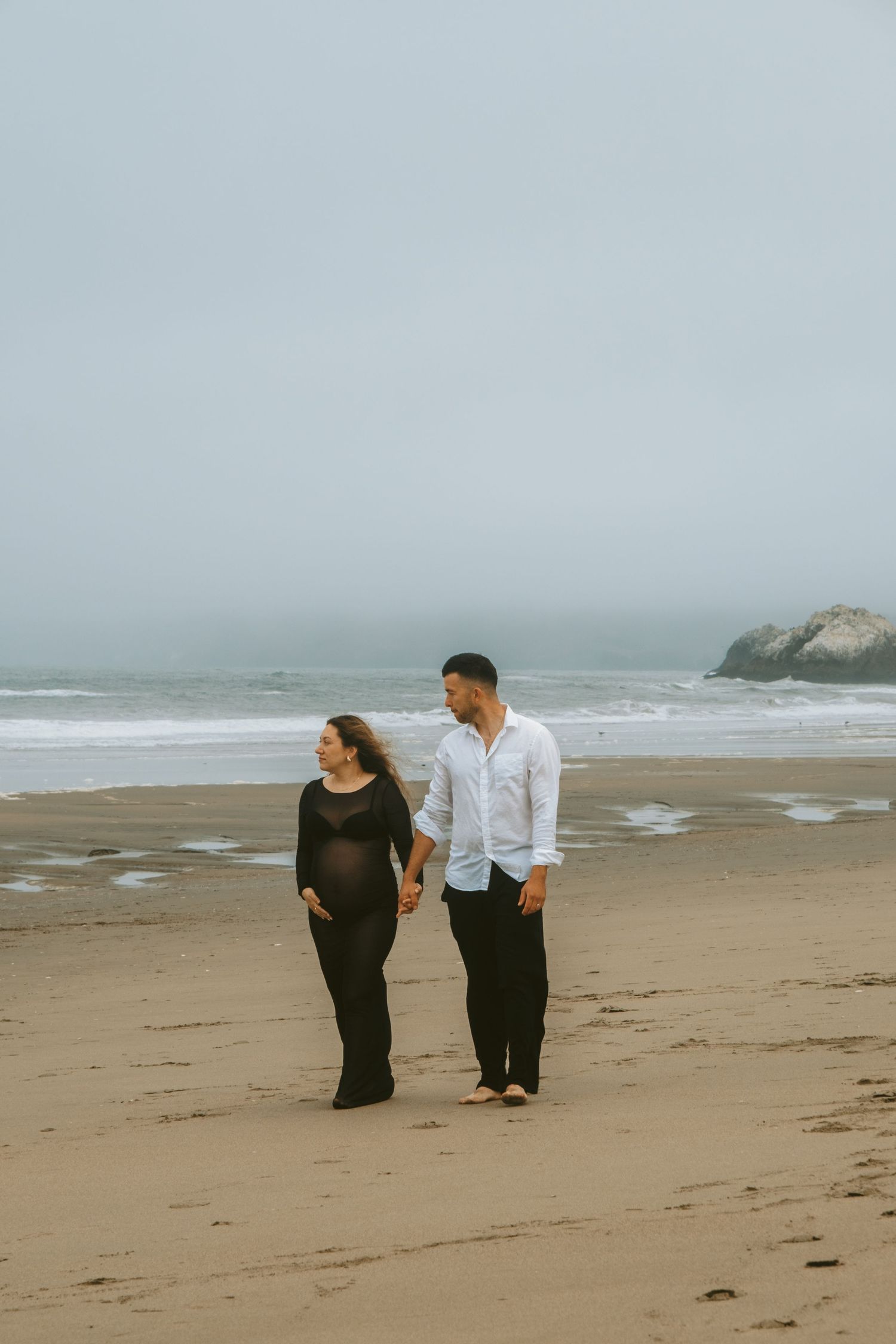 Couple walking and talking together on foggy beach shoreline.