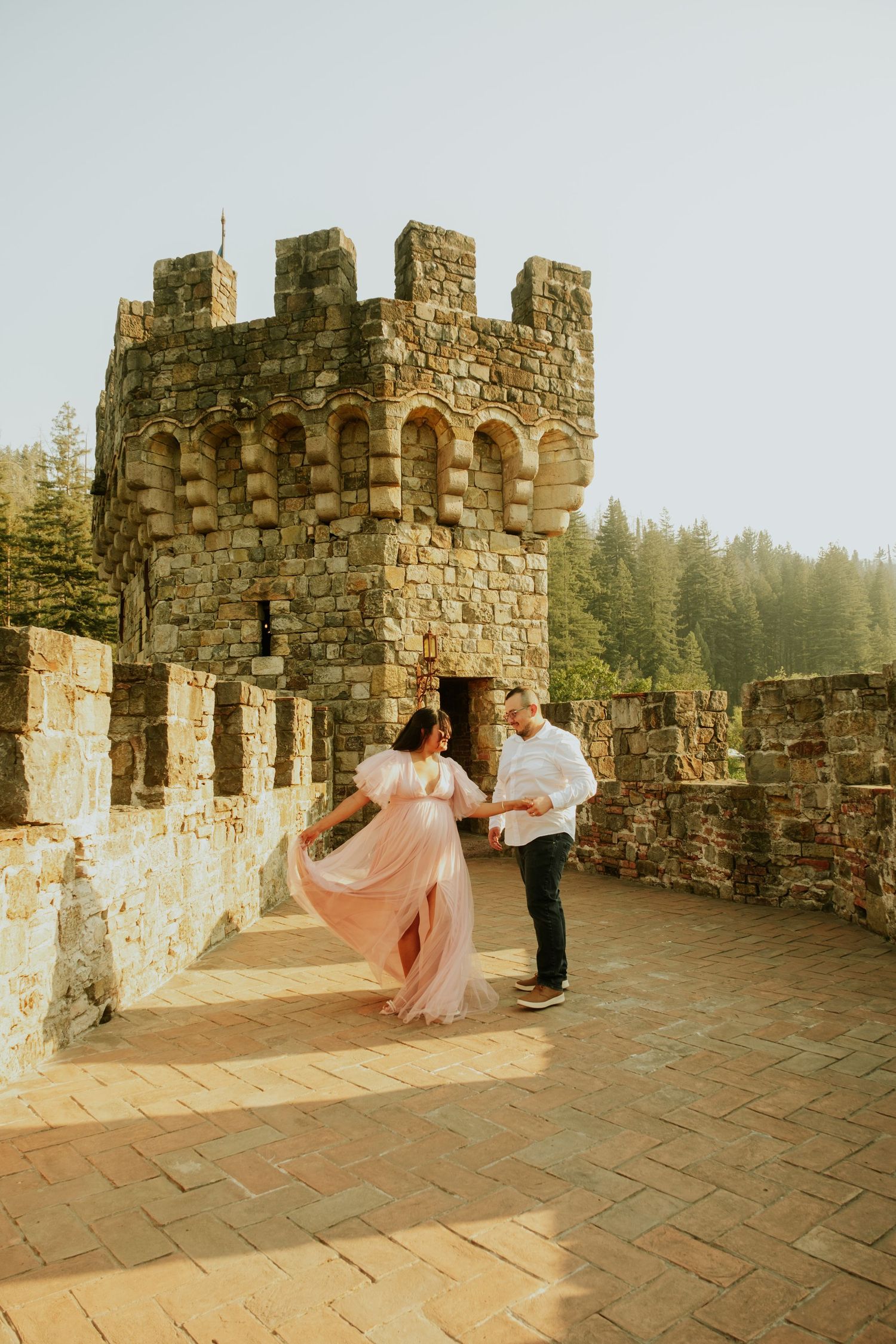 A couple dances on a castle's stone terrace during golden hour.