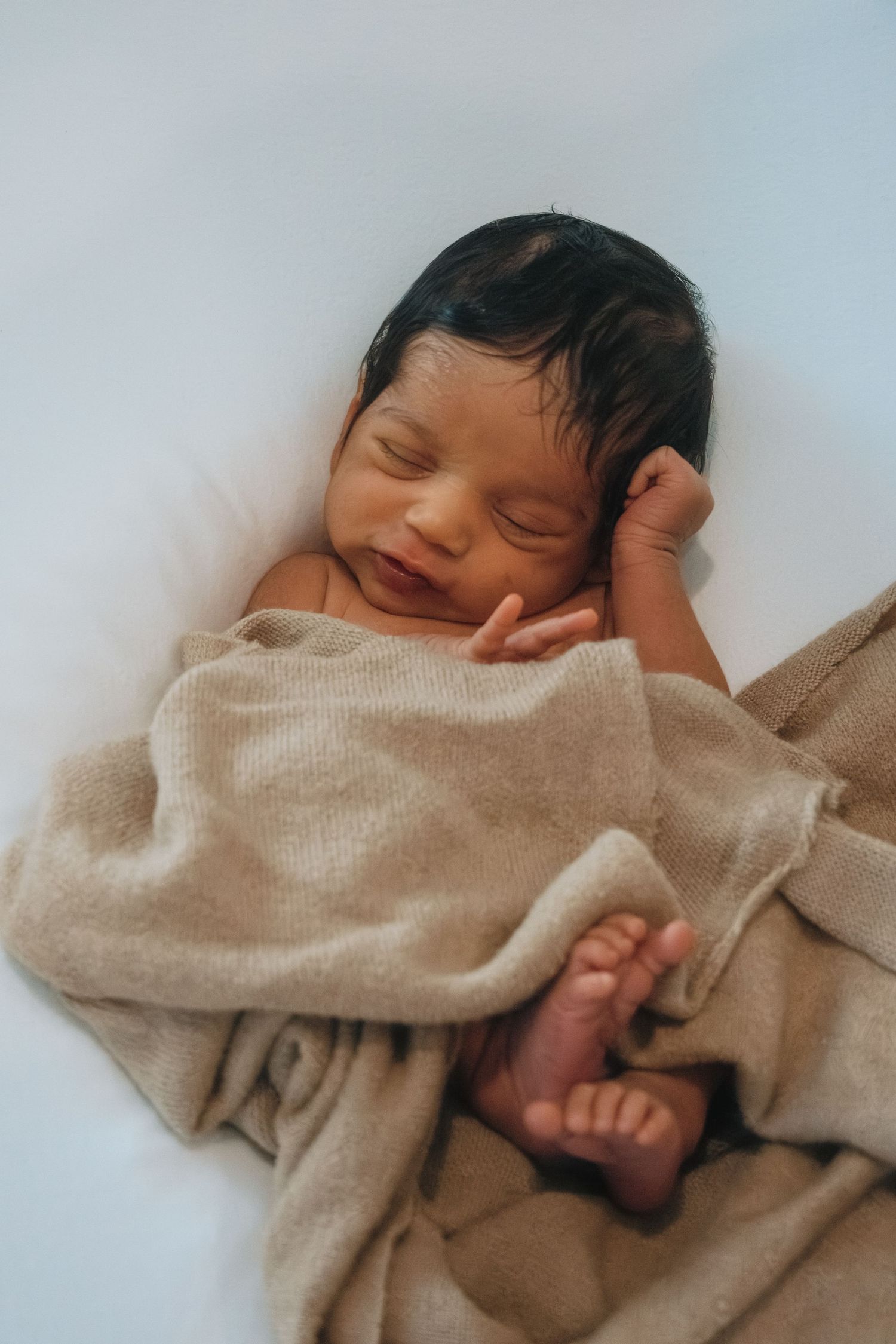 Peaceful sleeping baby wrapped in cozy beige knit blanket.