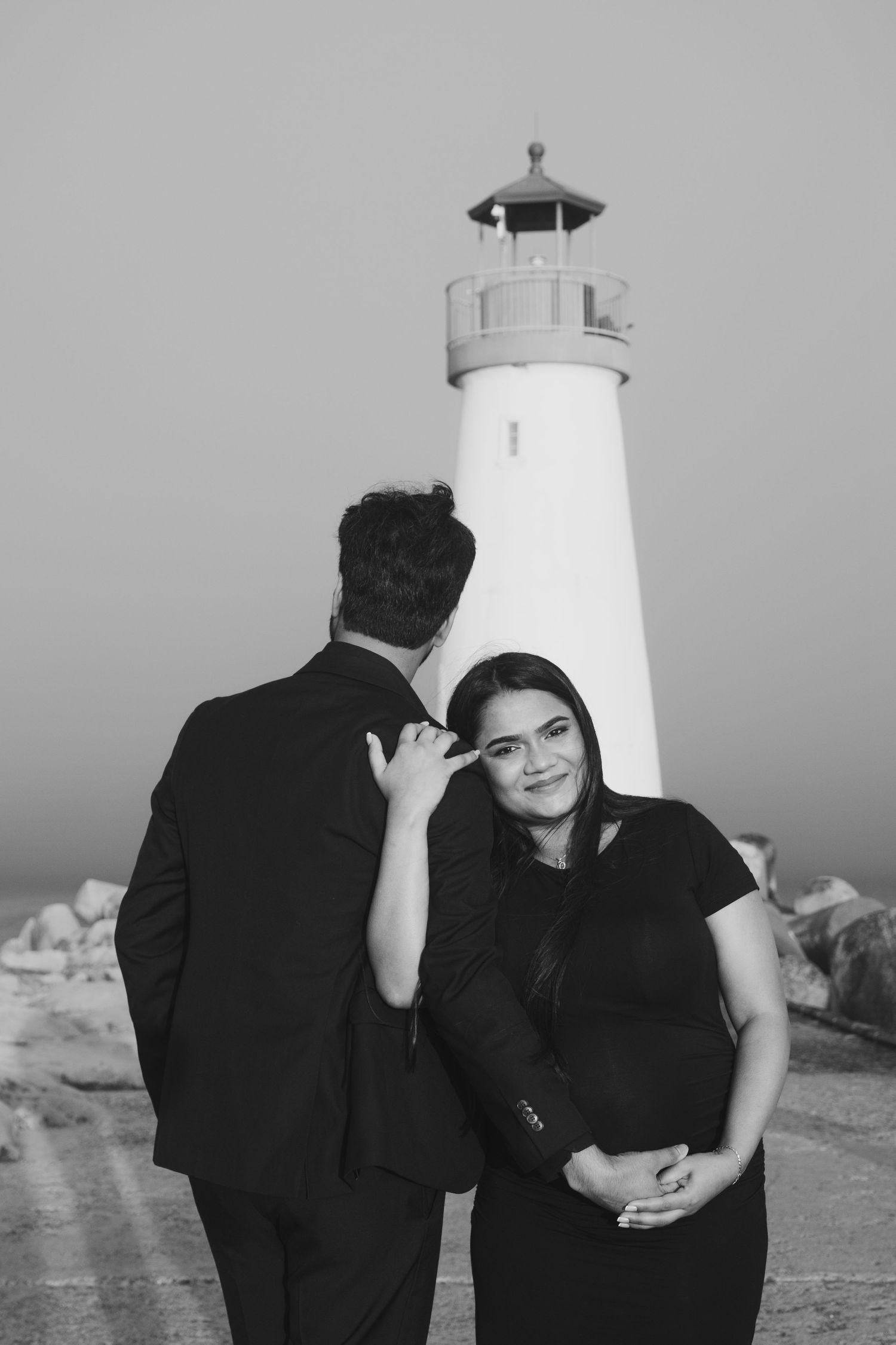 A couple shares playful moments near a lighthouse in monochrome.