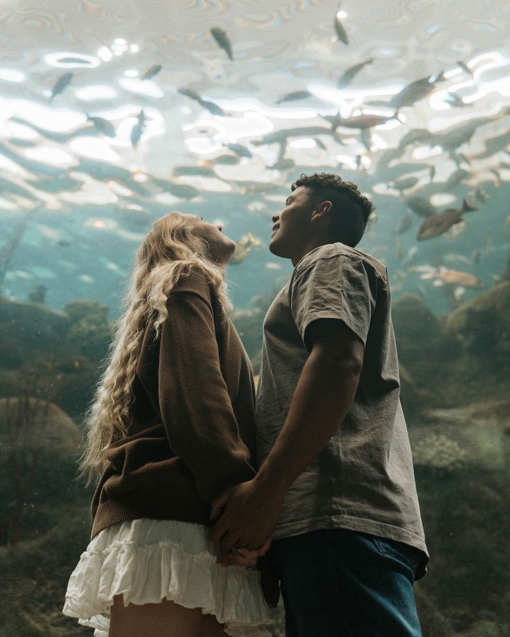 Couple holding hands beneath aquarium ceiling filled with swimming fish.