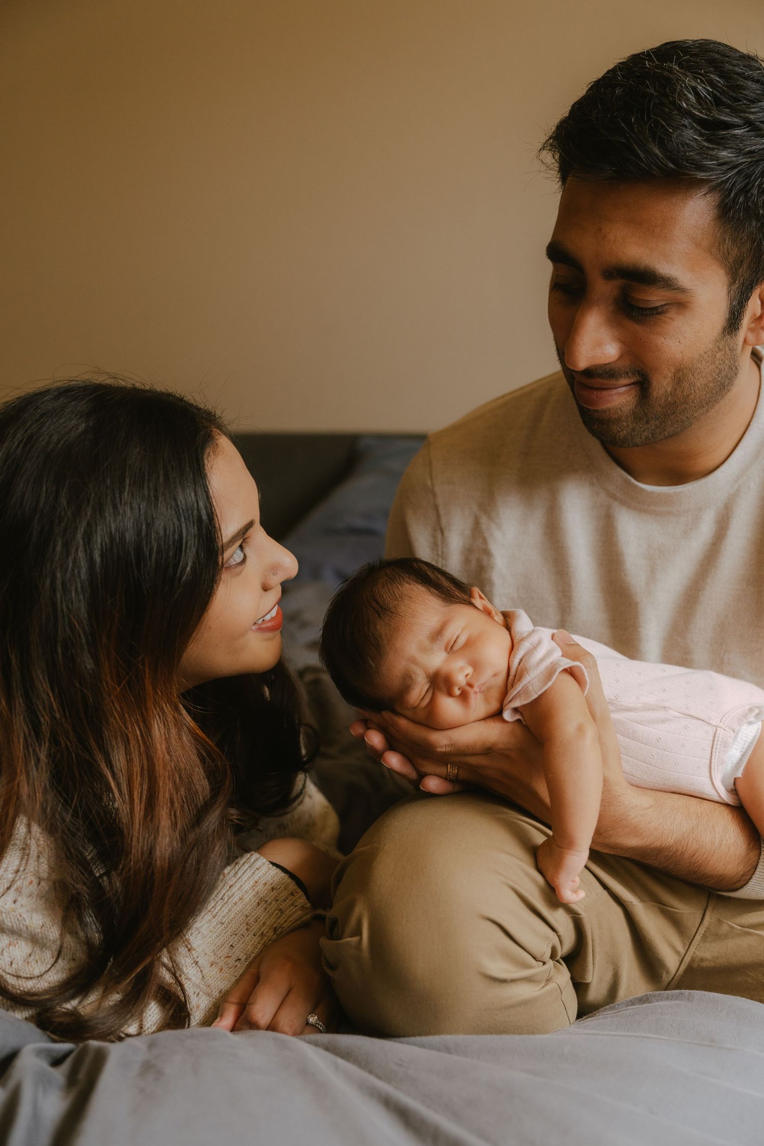 New parents smiling lovingly at their sleeping newborn baby, sharing a tender family moment together.