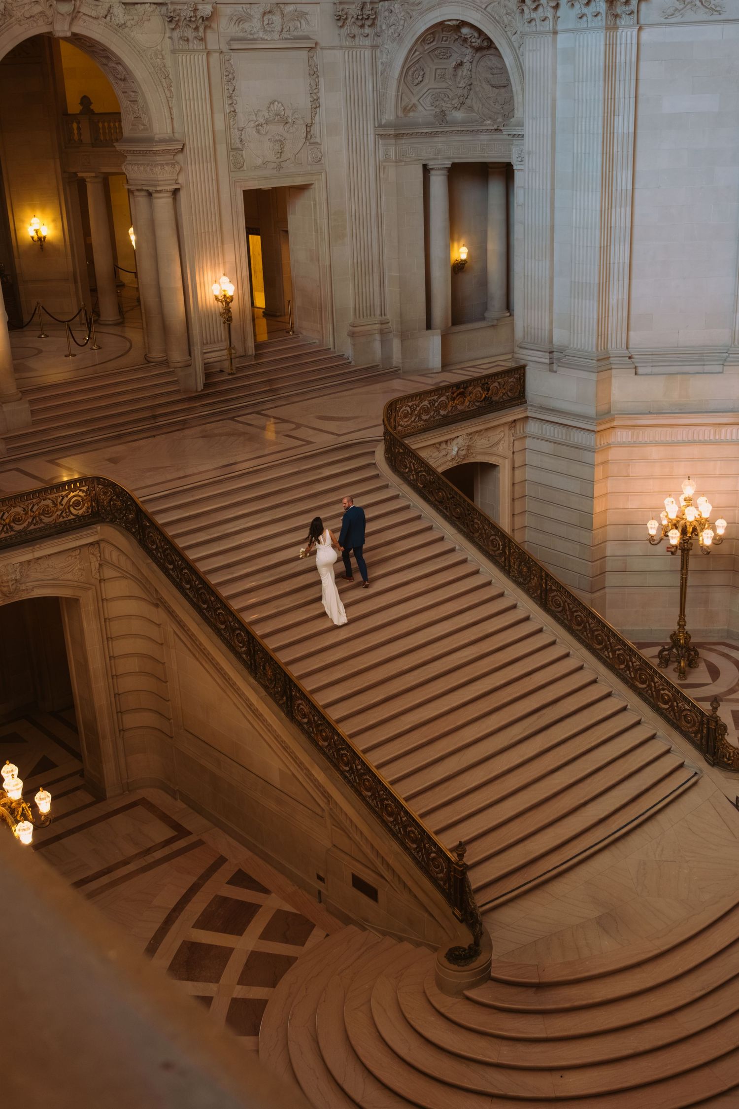 Elegant curved marble staircase with ornate railings and warm lighting in a grand historic building interior.