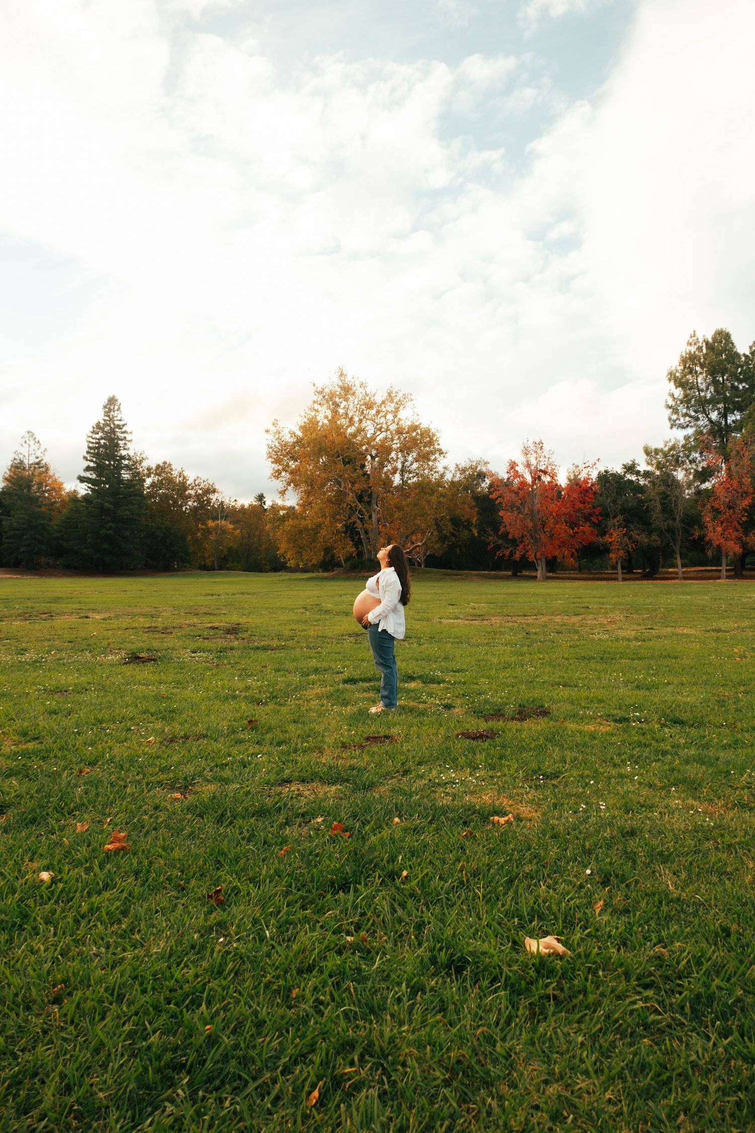 People walking across a grassy field during autumn with colorful trees in background.