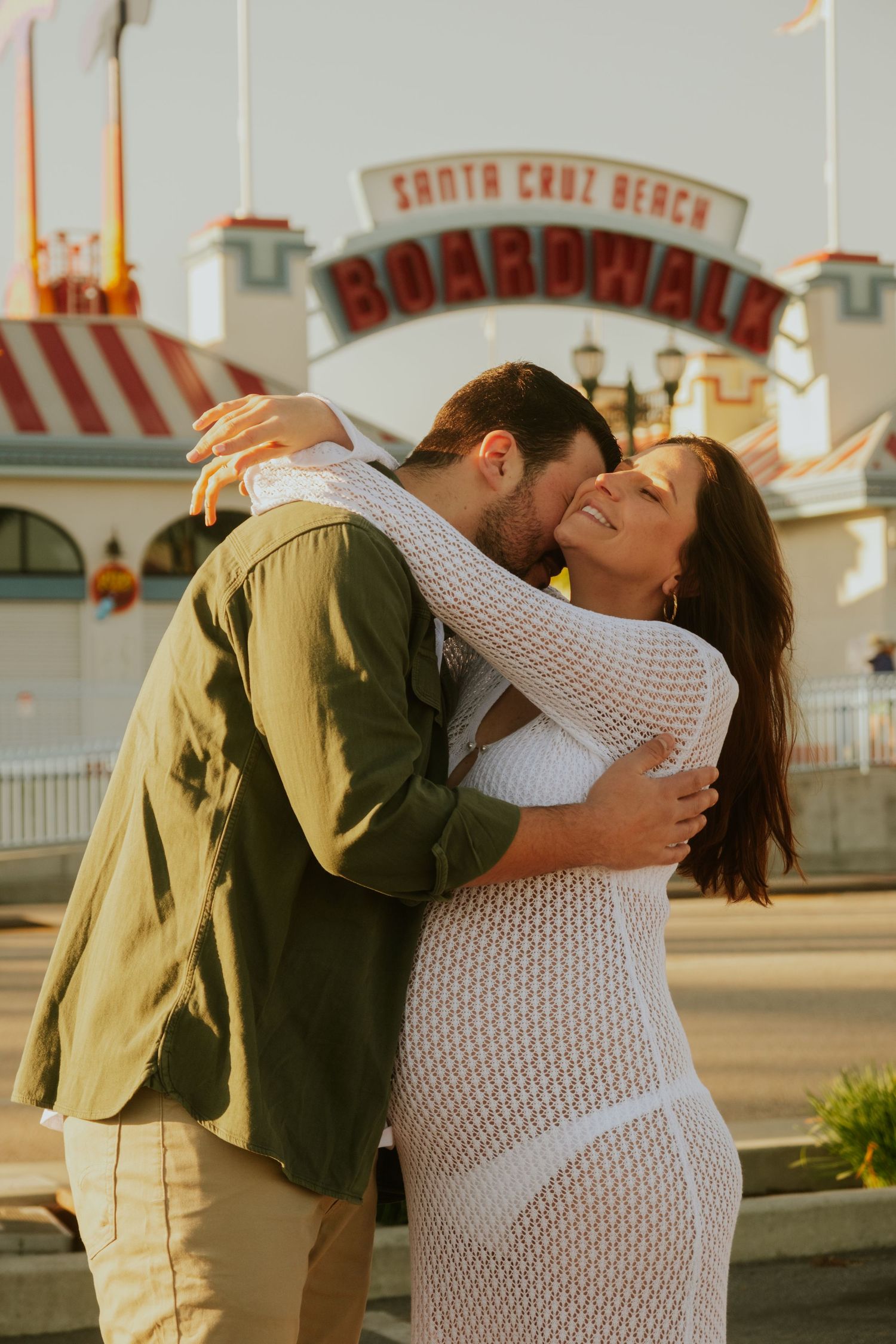 A romantic photoshoot sequence at a boardwalk with vintage carnival lights in the background.