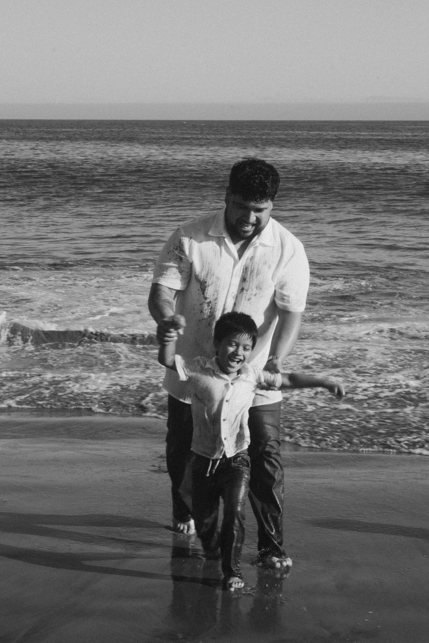 Black and white photo of playful interactions at the beach with waves in the background.