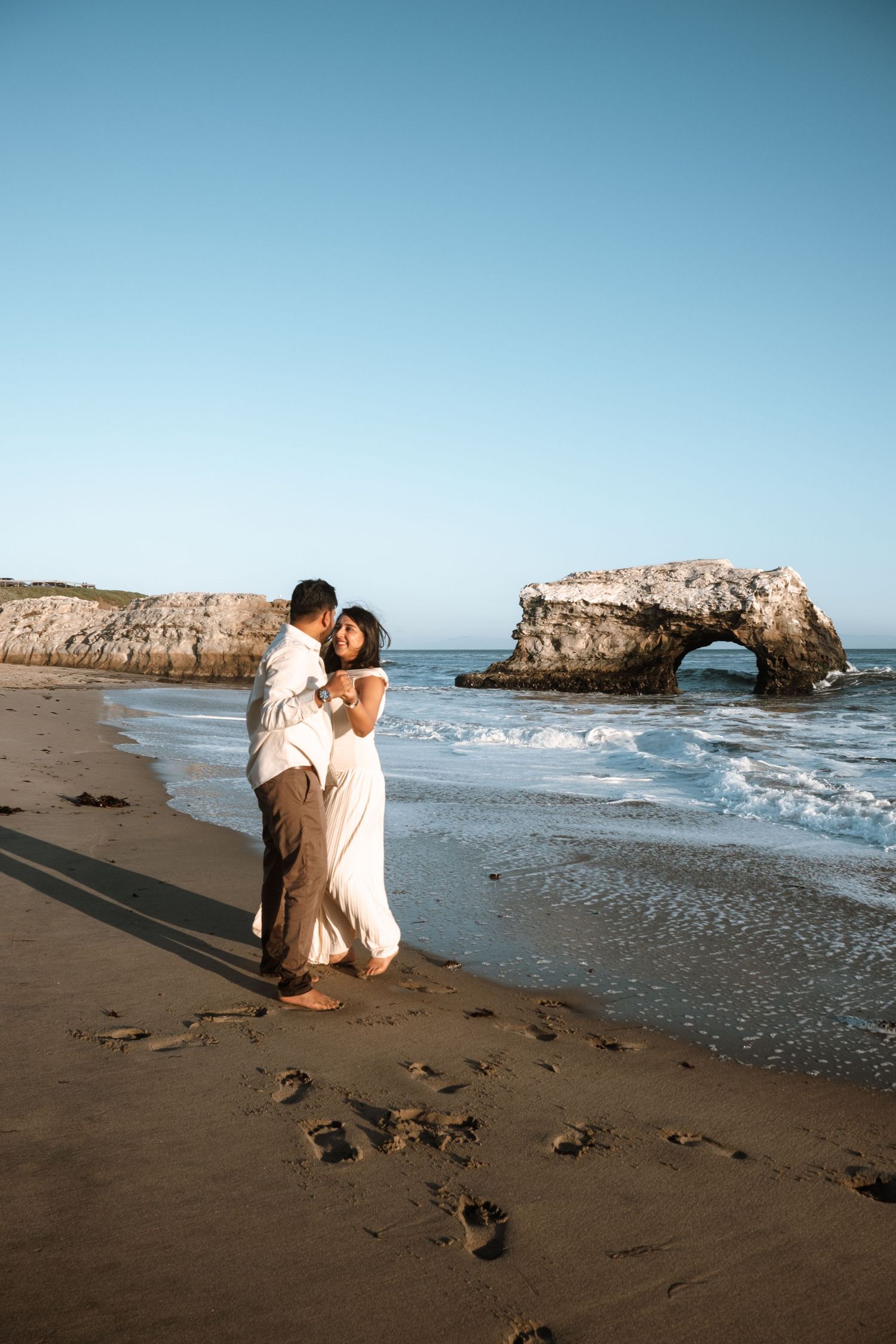 Photographer capturing shots on a sandy beach with dramatic rock formations in the background.