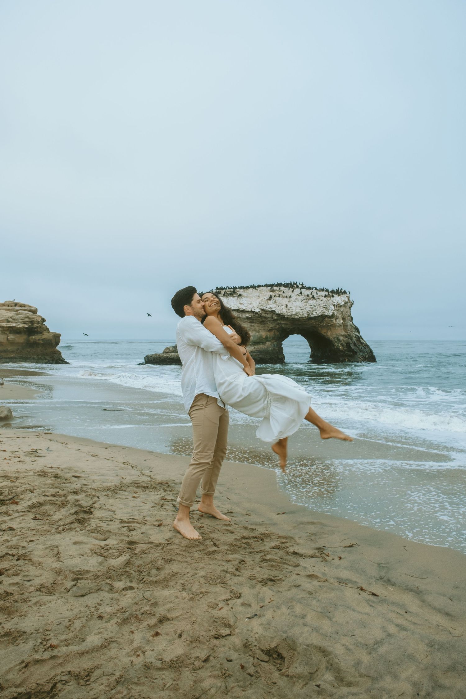 Playful beach photoshoot with natural rock arch formation in the background.