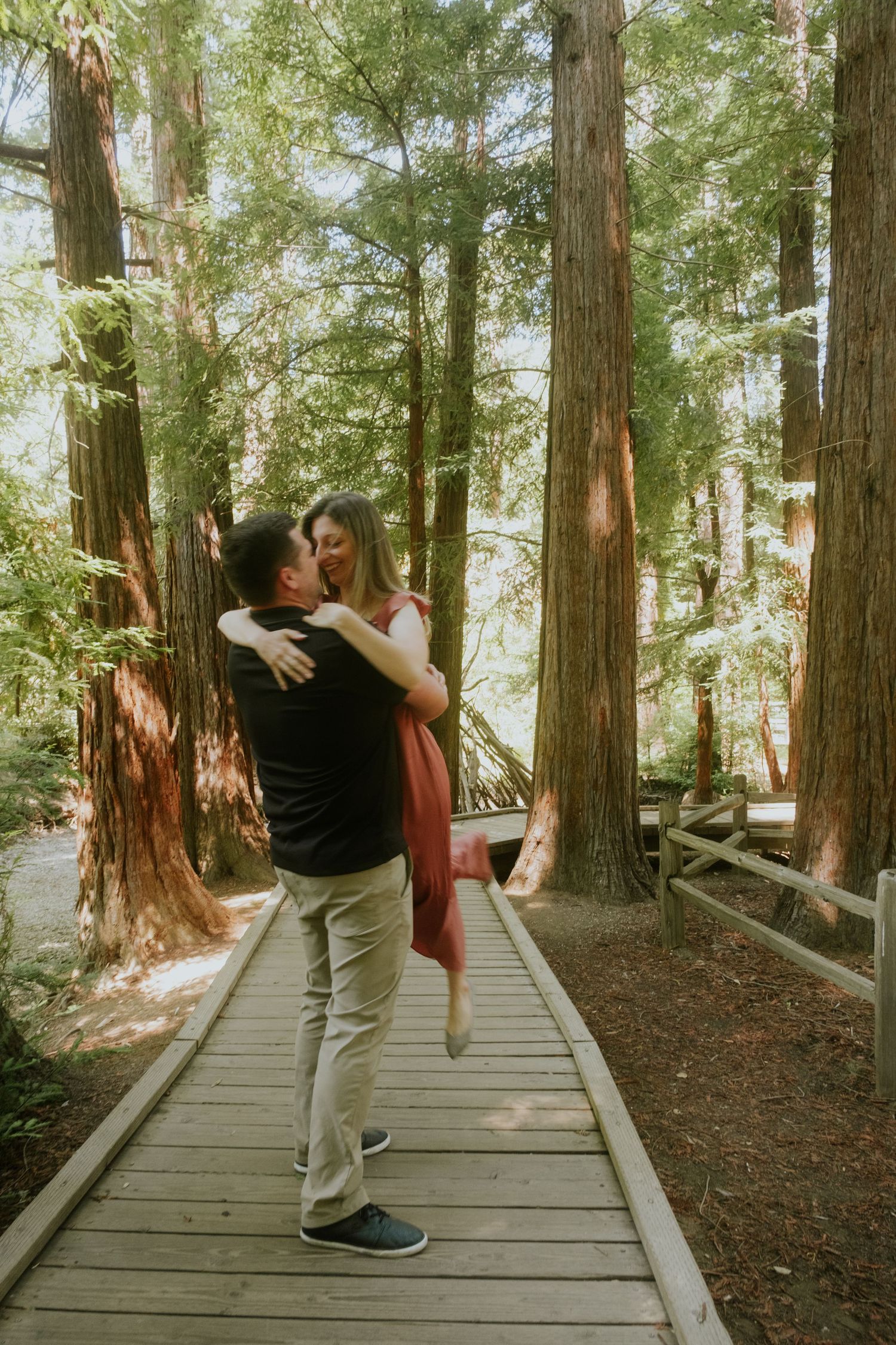 Couple dances and spins together on scenic forest boardwalk among tall trees.