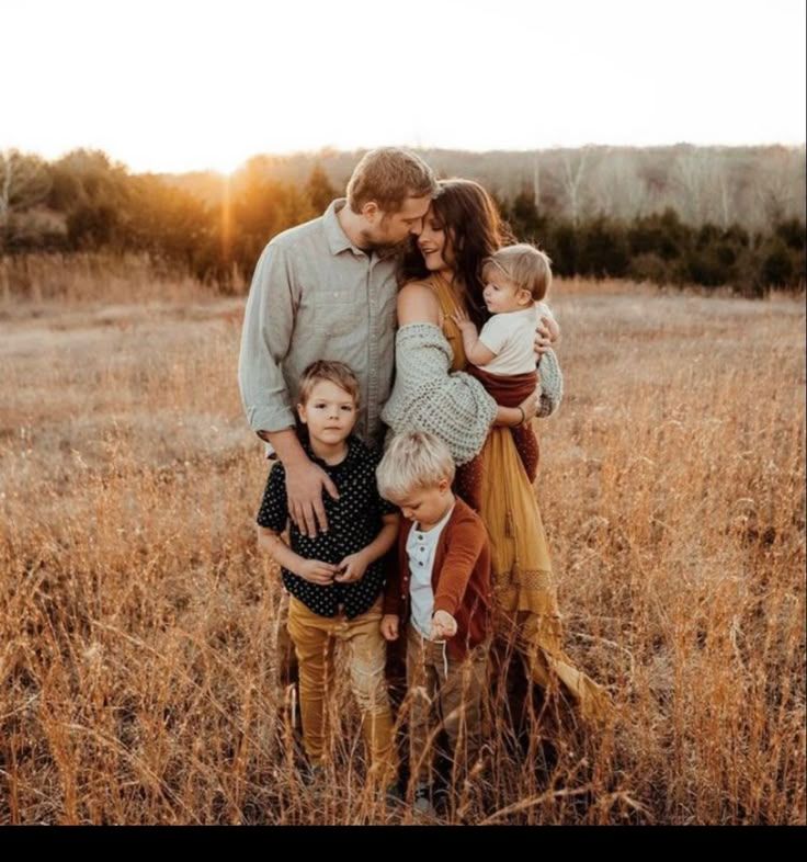 Family of four posing together in rustic field during golden hour.