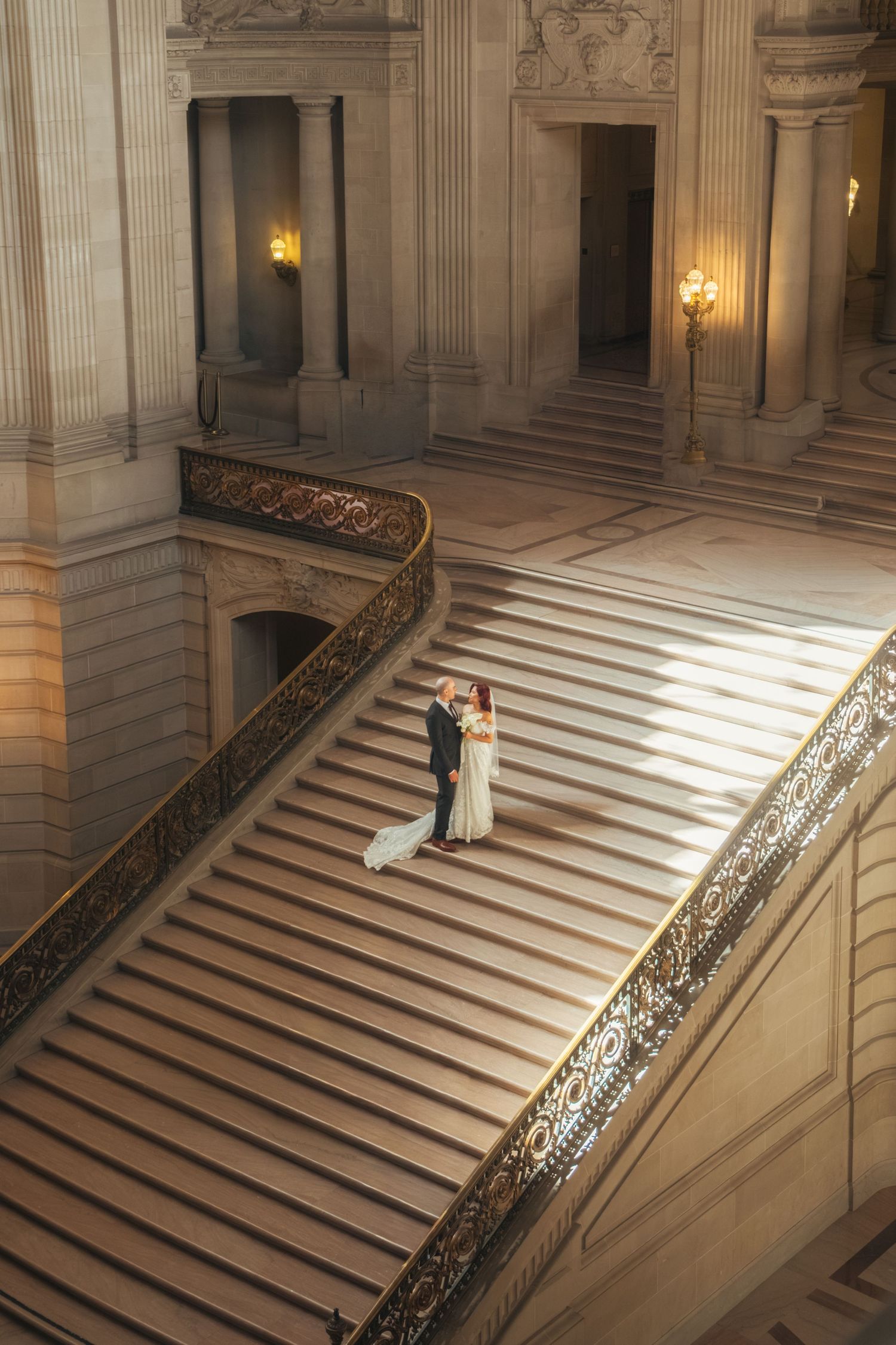 Sunlight streams across a grand marble staircase during an intimate moment.