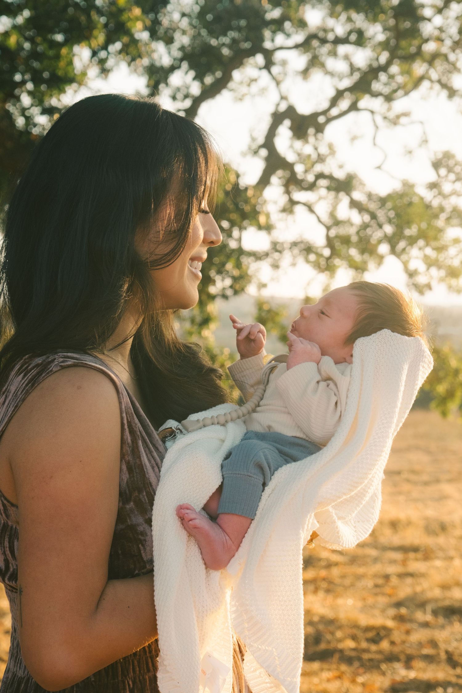 Sweet bonding moment with infant wrapped in white blanket during sunset photoshoot.