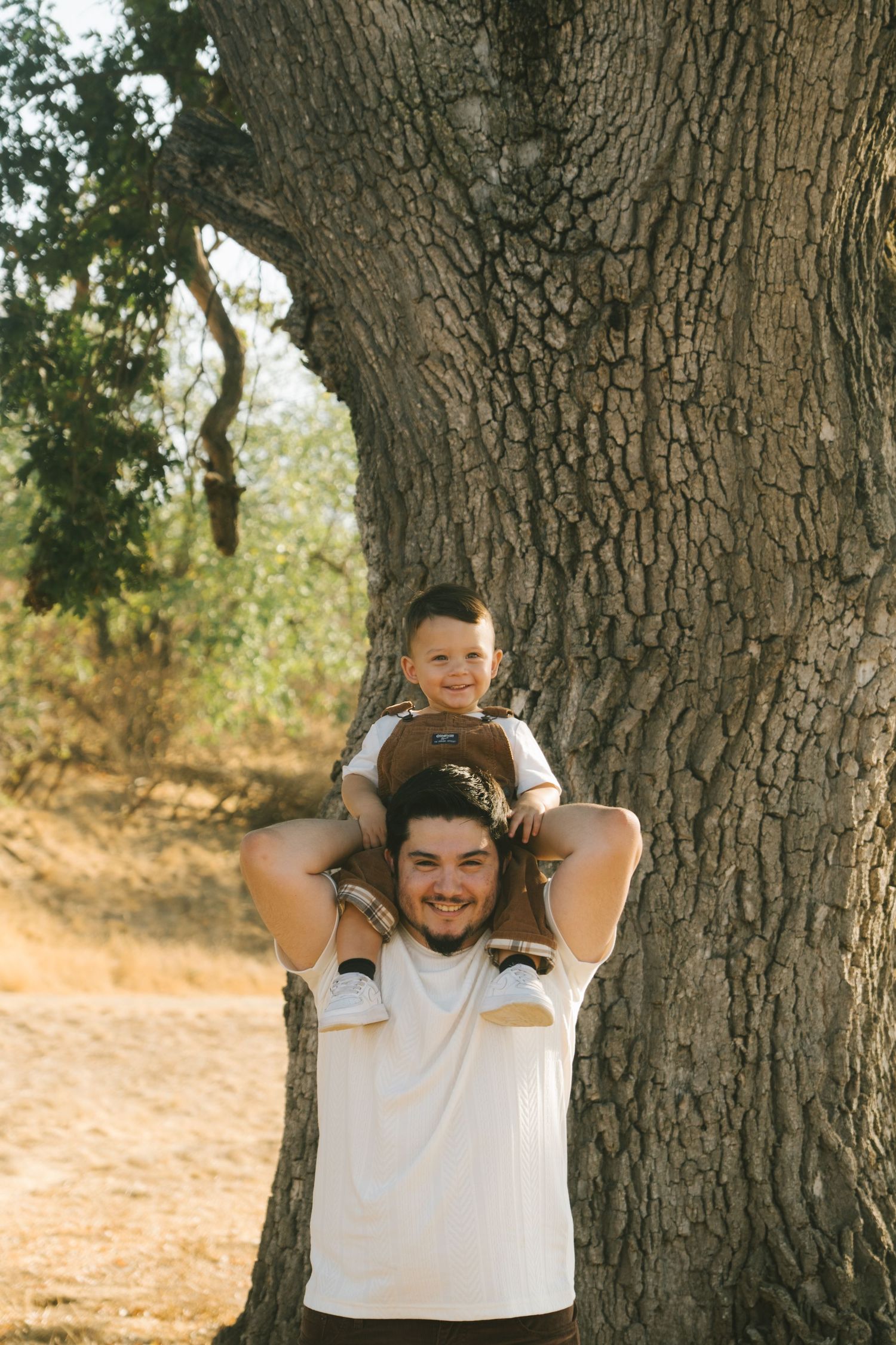Joyful moments captured under large tree trunk during outdoor photoshoot.