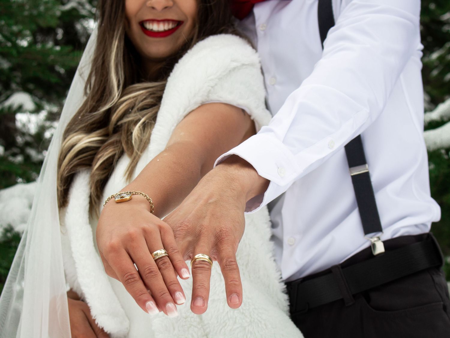 Close-up of newlyweds showing off wedding rings against snowy winter backdrop.