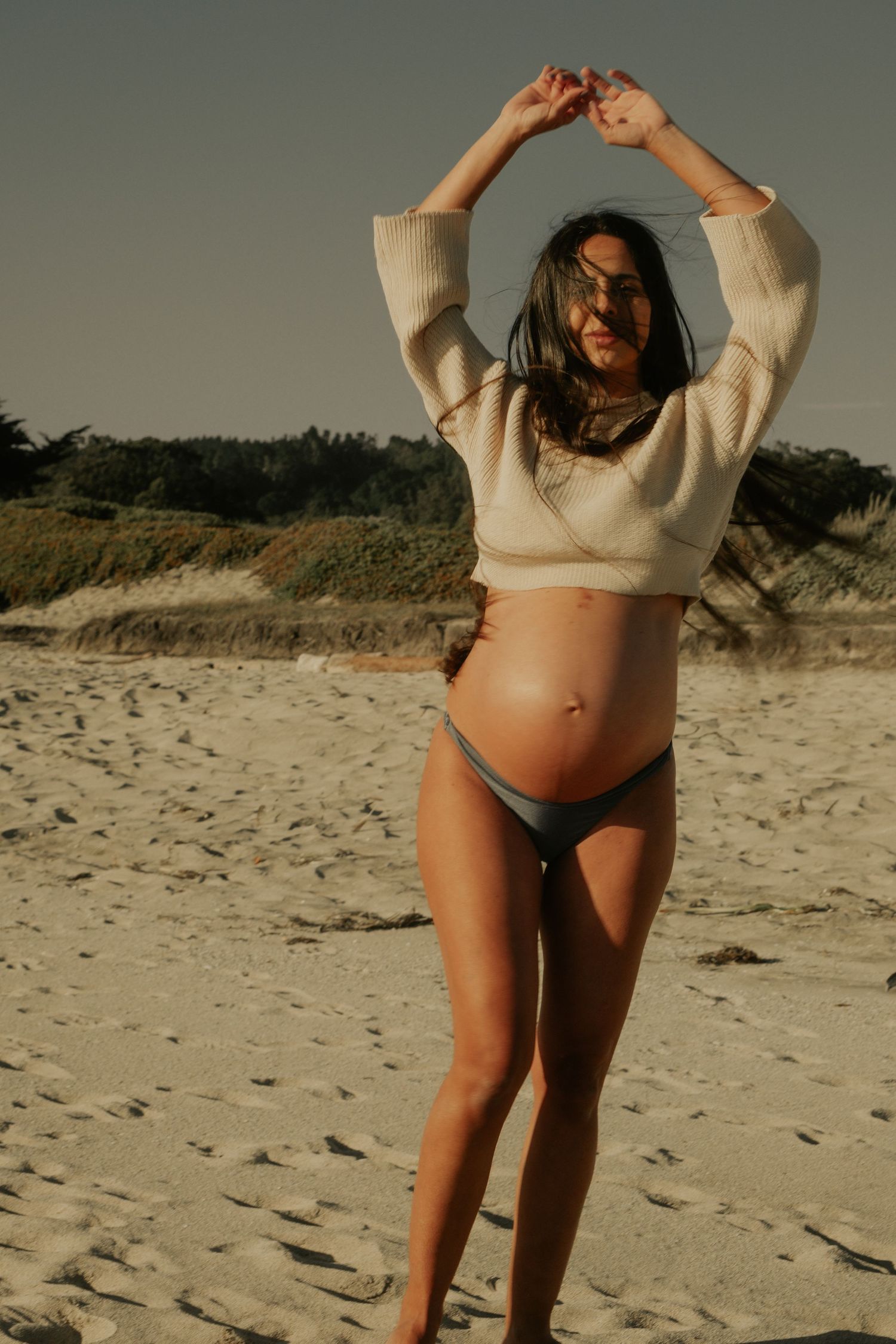 Figure in casual beachwear posing on sandy beach during golden hour.