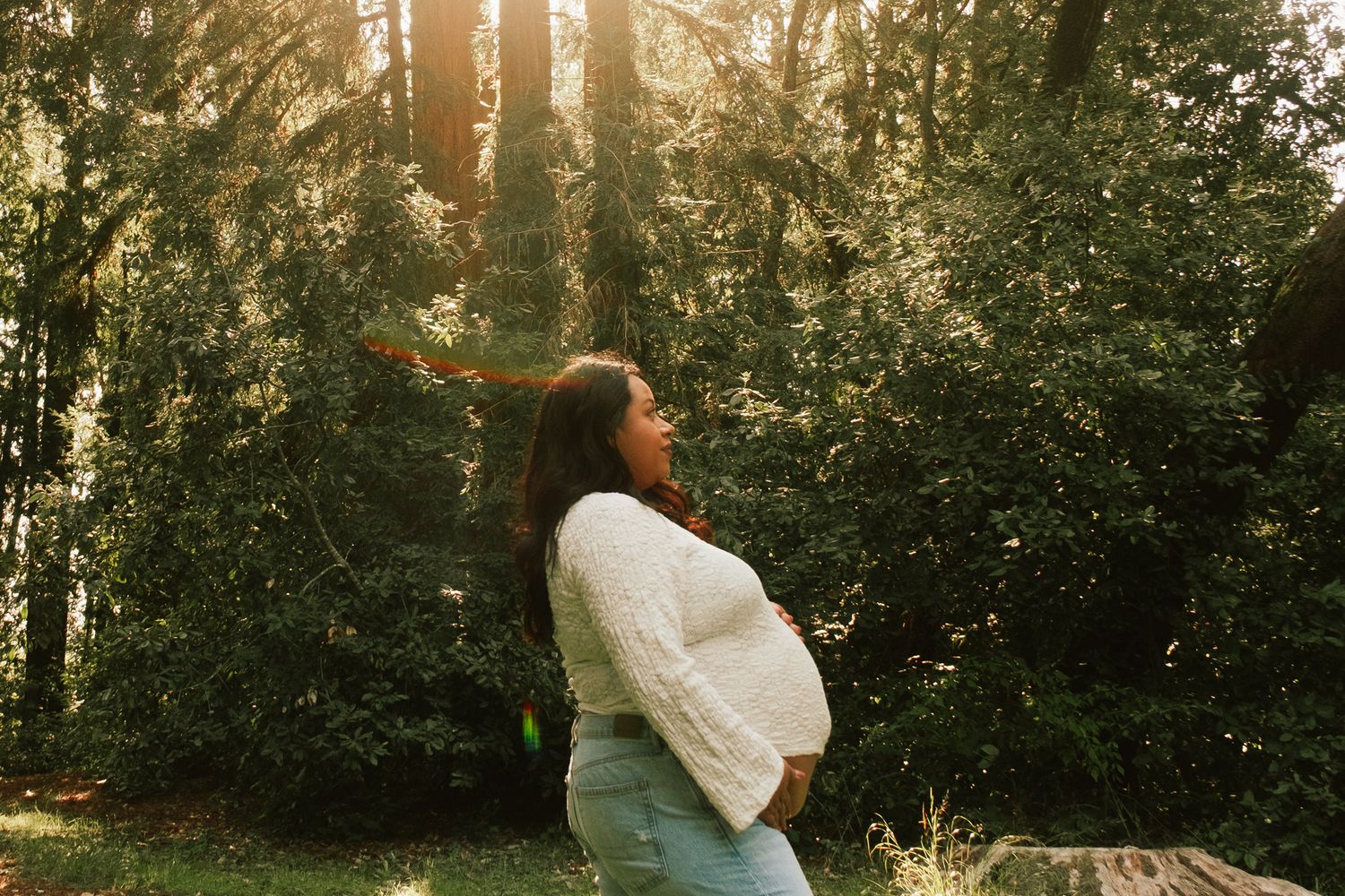 Couple walking through sunlit forest during golden hour photoshoot.