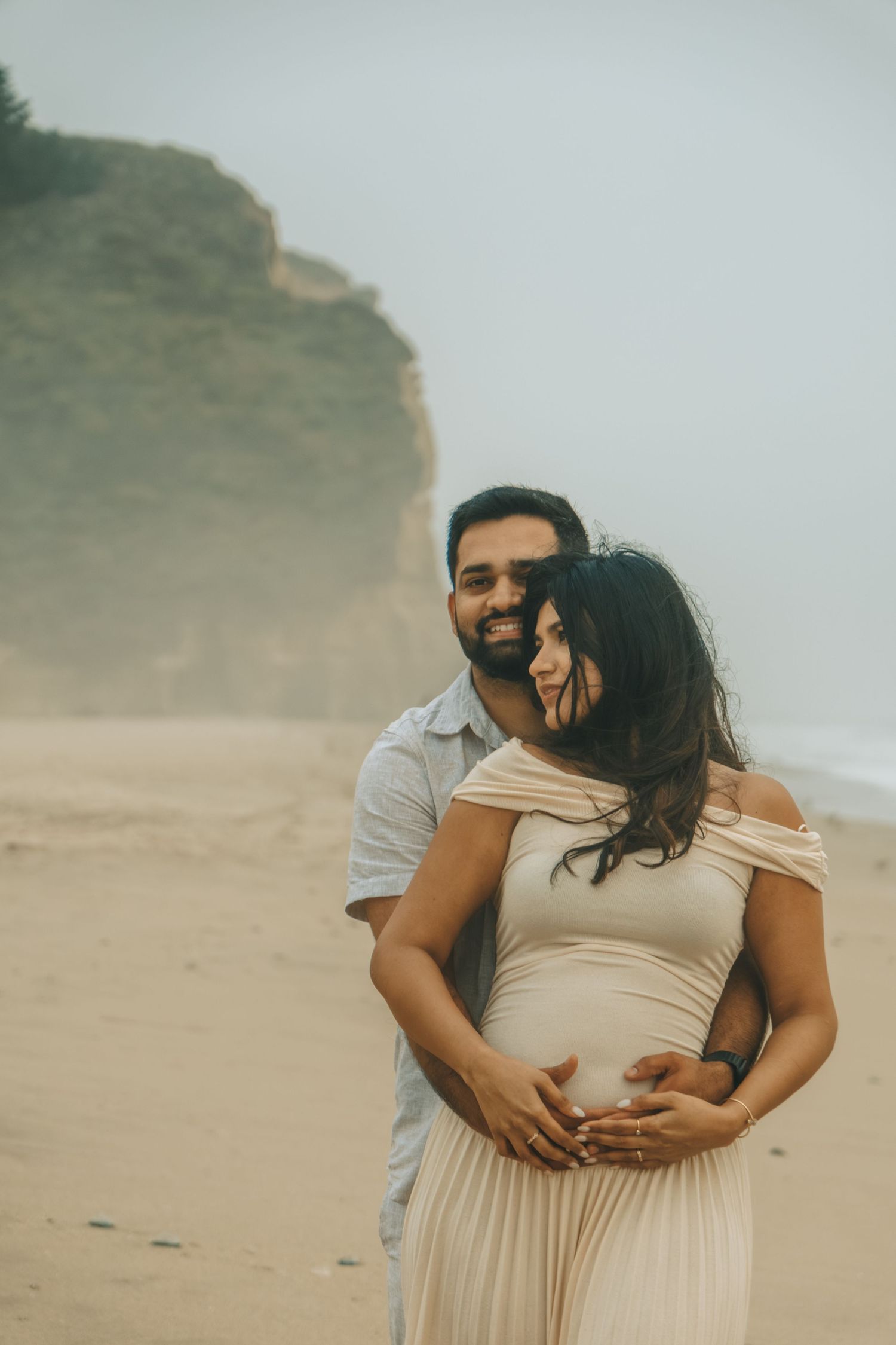 Couple embracing on misty beach with coastal cliffs in background.