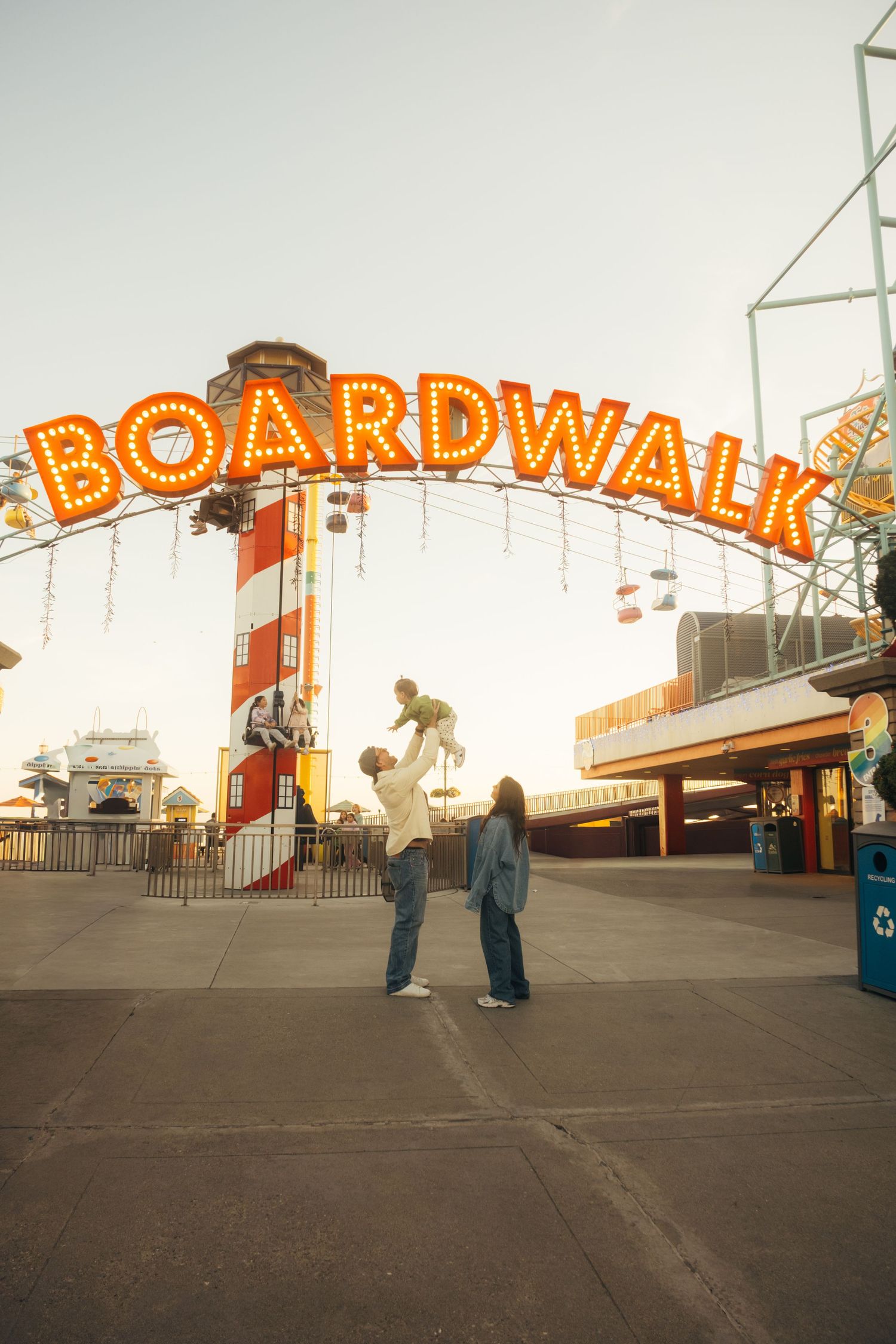Family enjoying a sunny day under the illuminated Boardwalk sign at a classic amusement park.