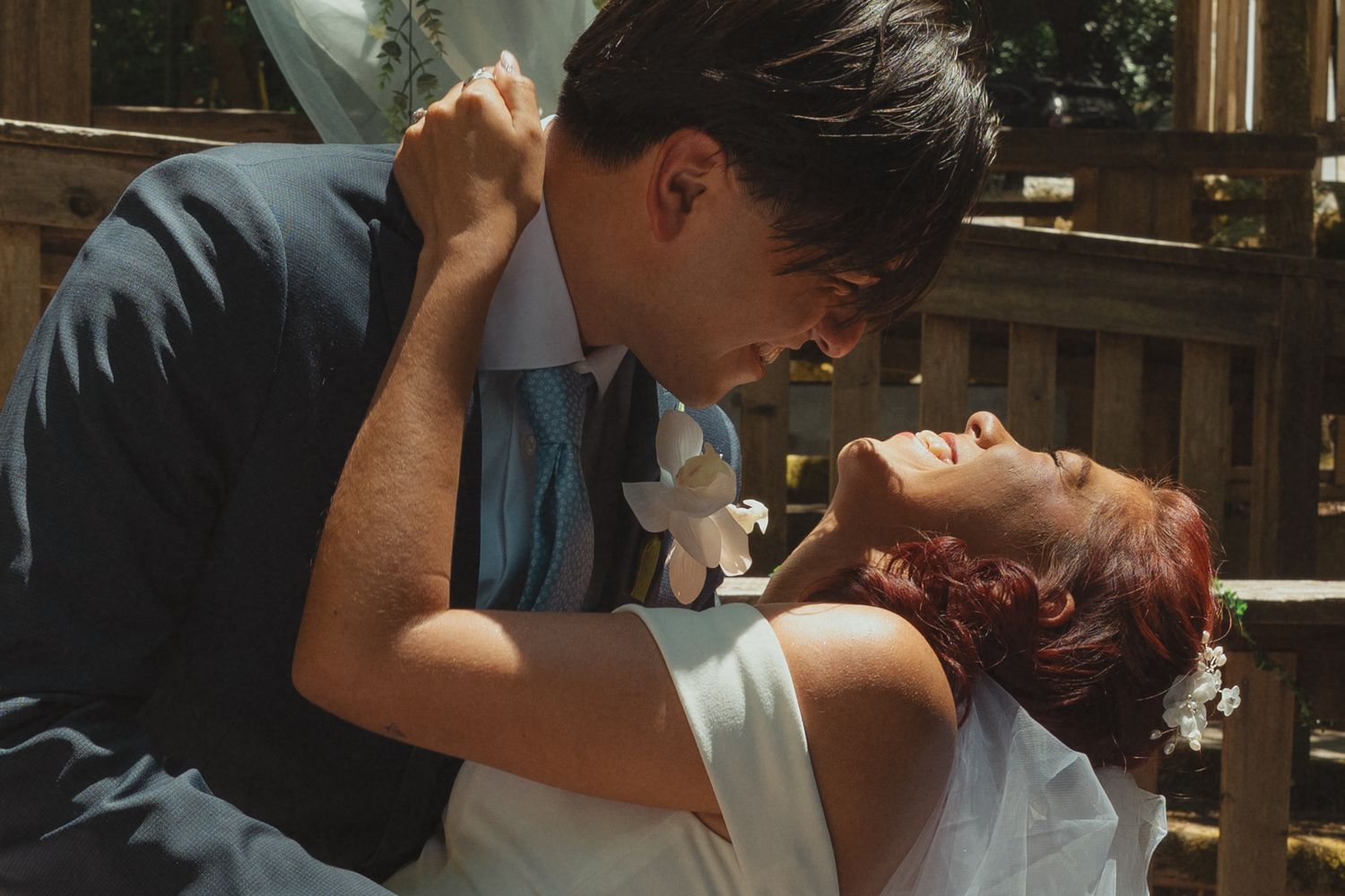 A bride and groom share a romantic moment outdoors, with the bride in white and groom in a blue suit.