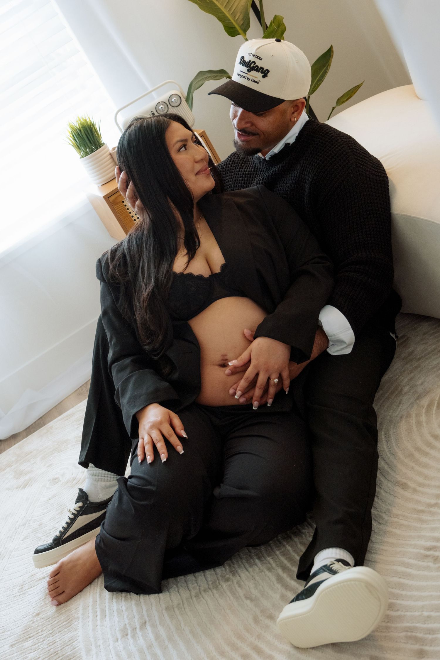 A couple in black outfits share intimate moments while sitting together on a white couch.