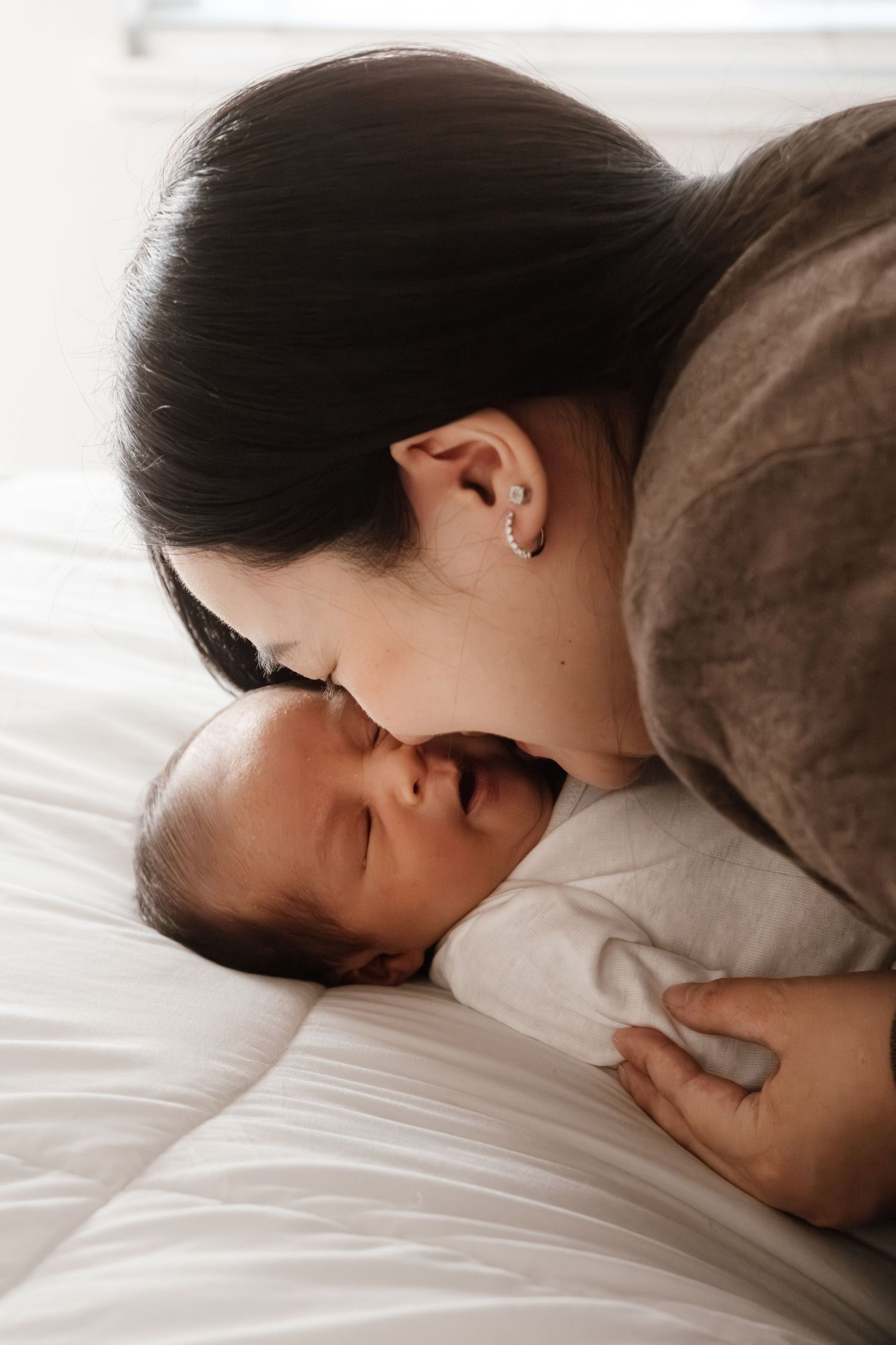 A series of intimate black and white photos showing tender moments of parent and baby resting together on white bedding.
