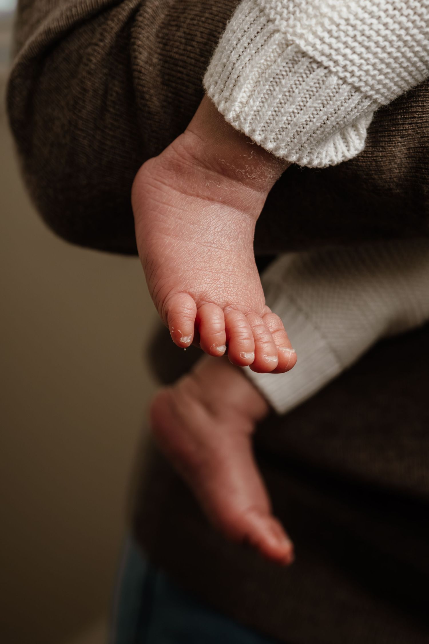 Close-up view of a tiny baby foot with a white knit sweater sleeve visible against a dark background.