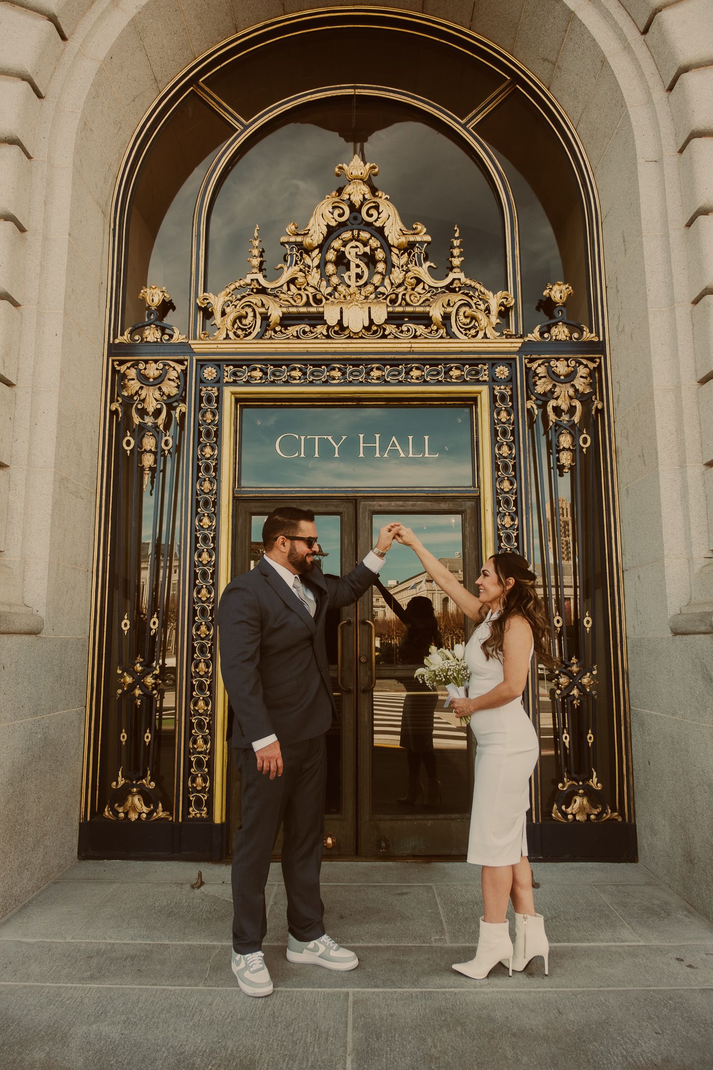 A couple stands in front of ornate golden City Hall doors during their intimate wedding ceremony.