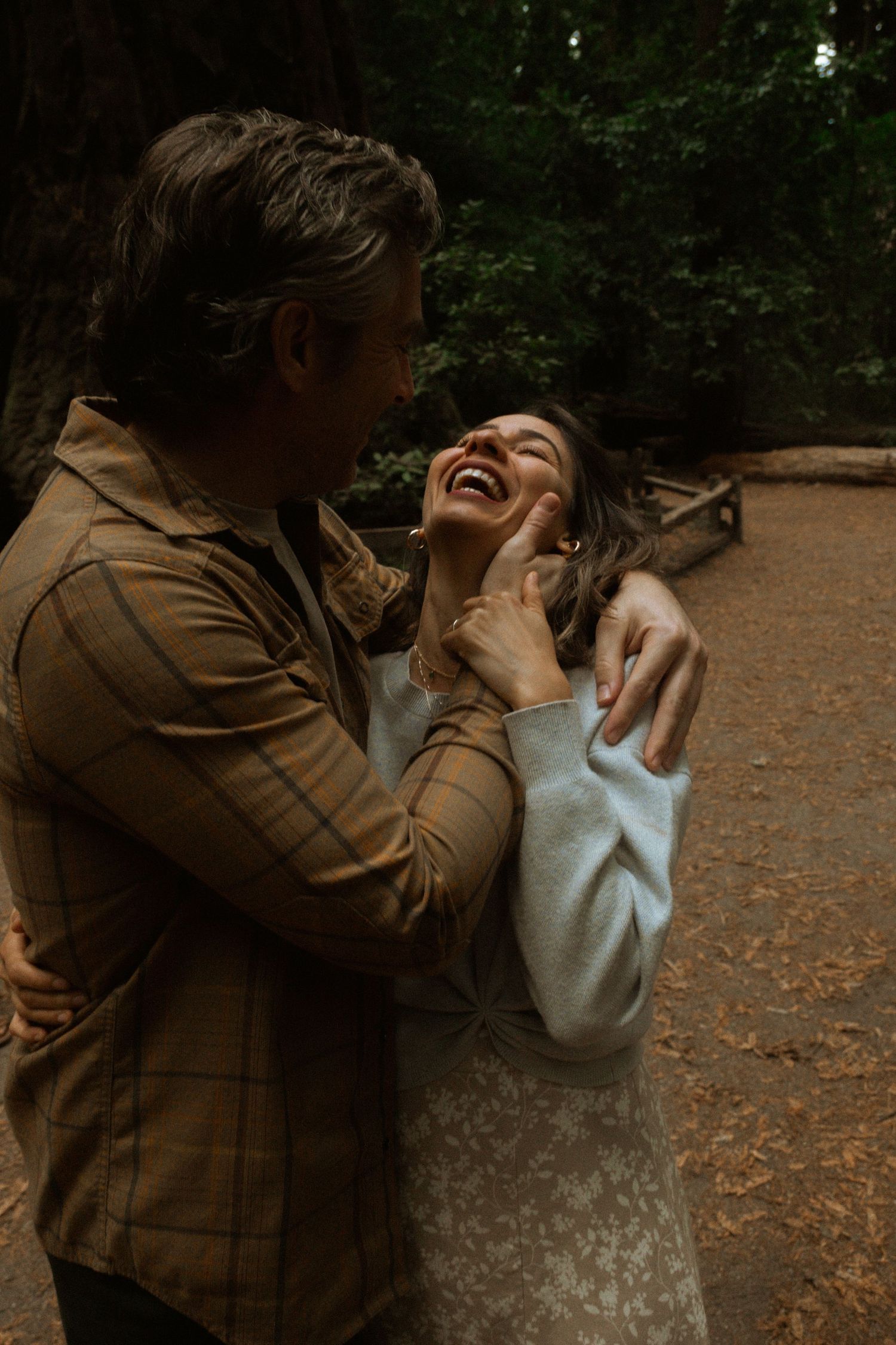 A playful moment captured between two people in a redwood forest.
