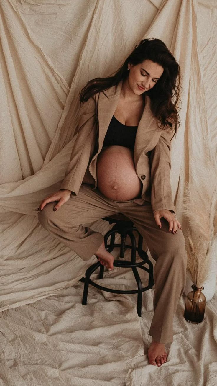 Artistic maternity photos with pregnant woman in beige coat on draped fabric backdrop.
