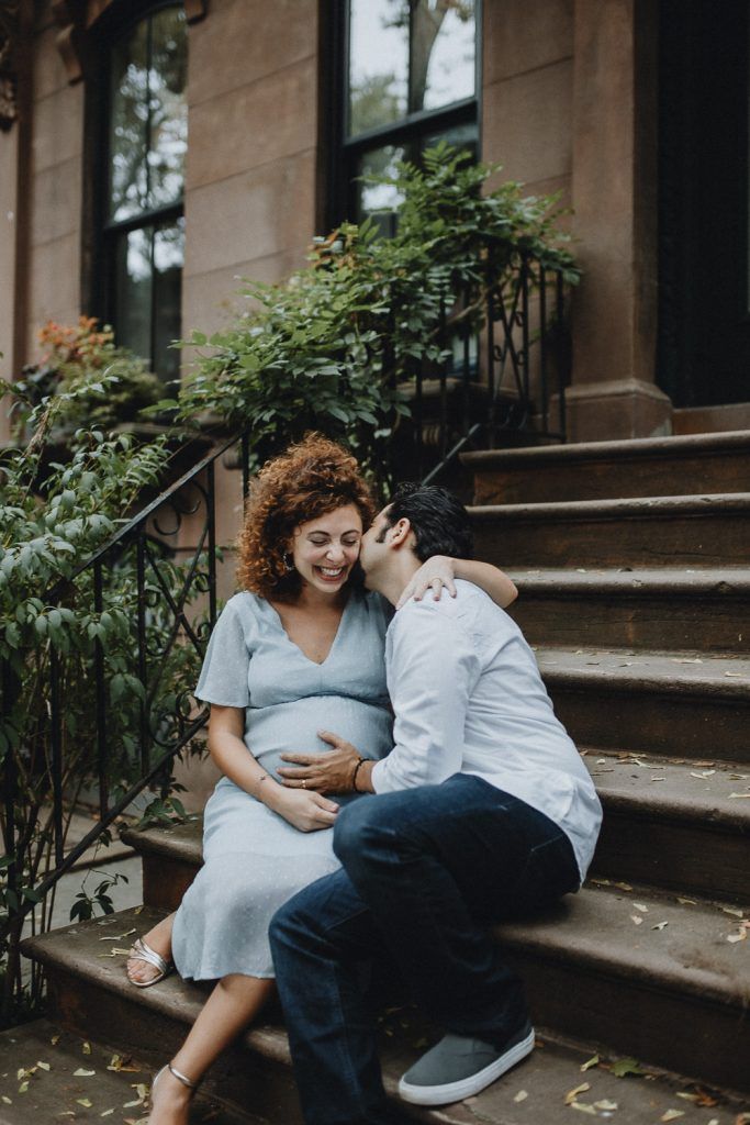 Expectant couple sharing tender moments on brownstone steps with scattered leaves.
