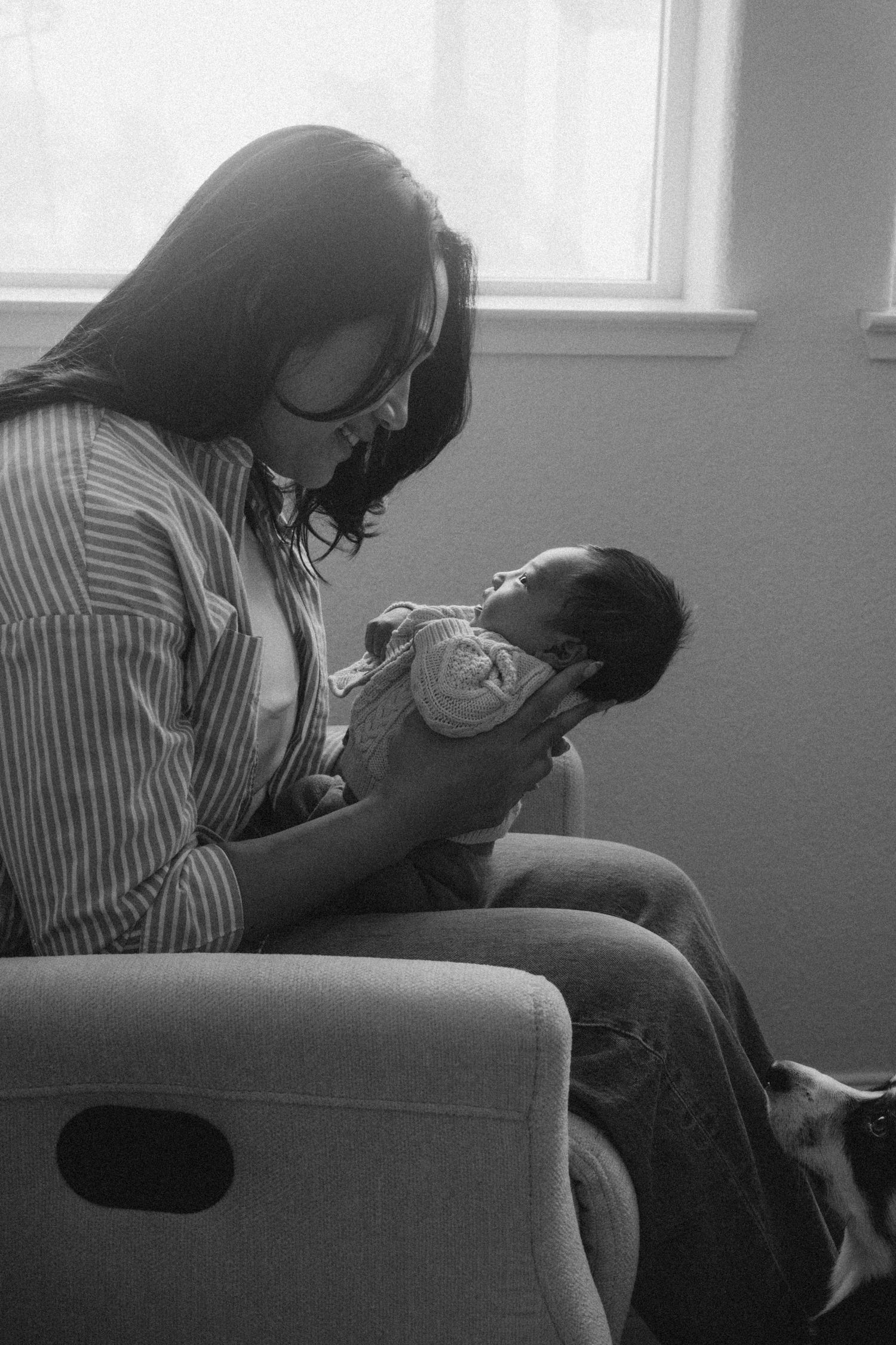 Black and white photo of a mother sitting in a chair lovingly gazing at her newborn baby.
