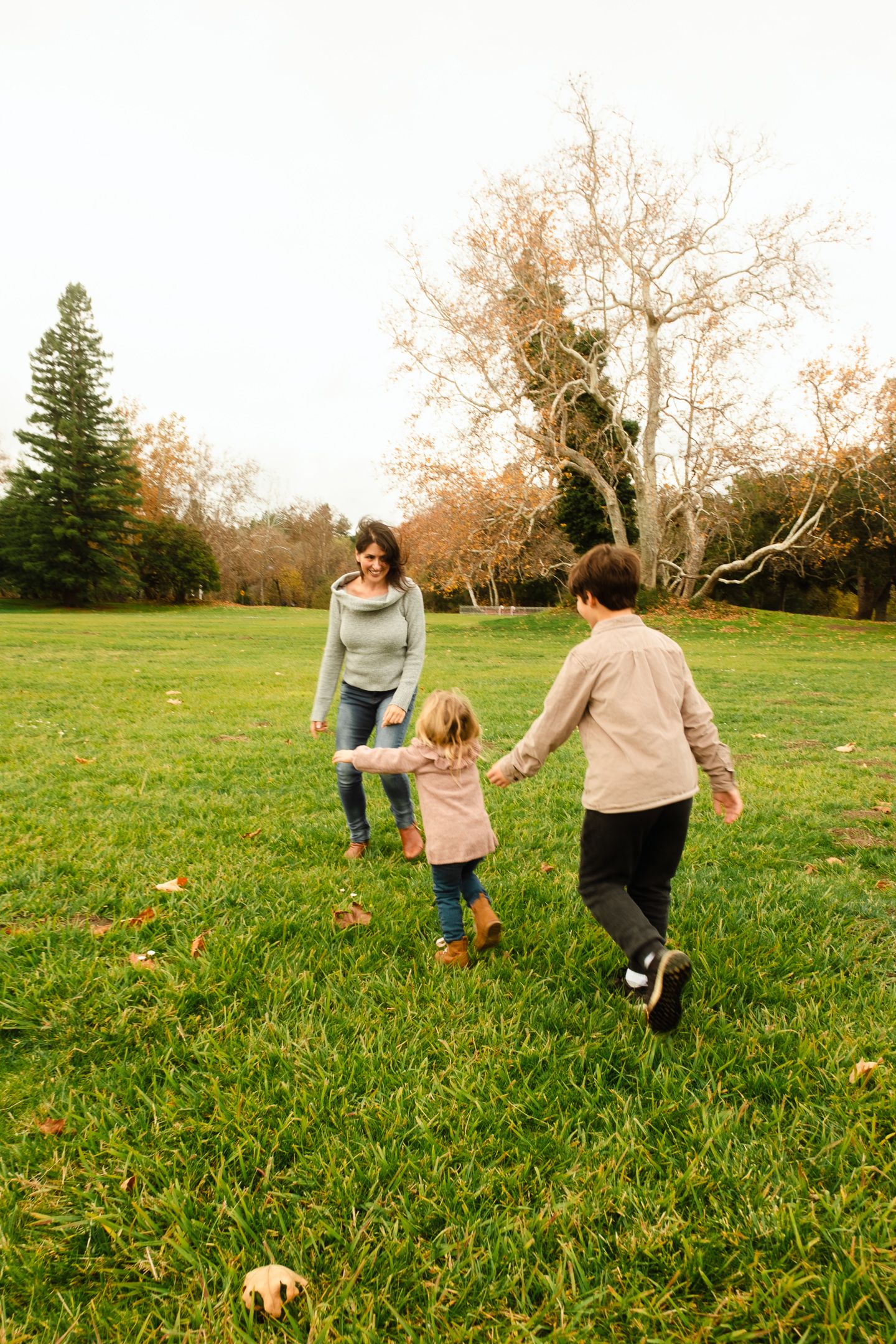 Family running together through a grassy field with their dog on an autumn day.