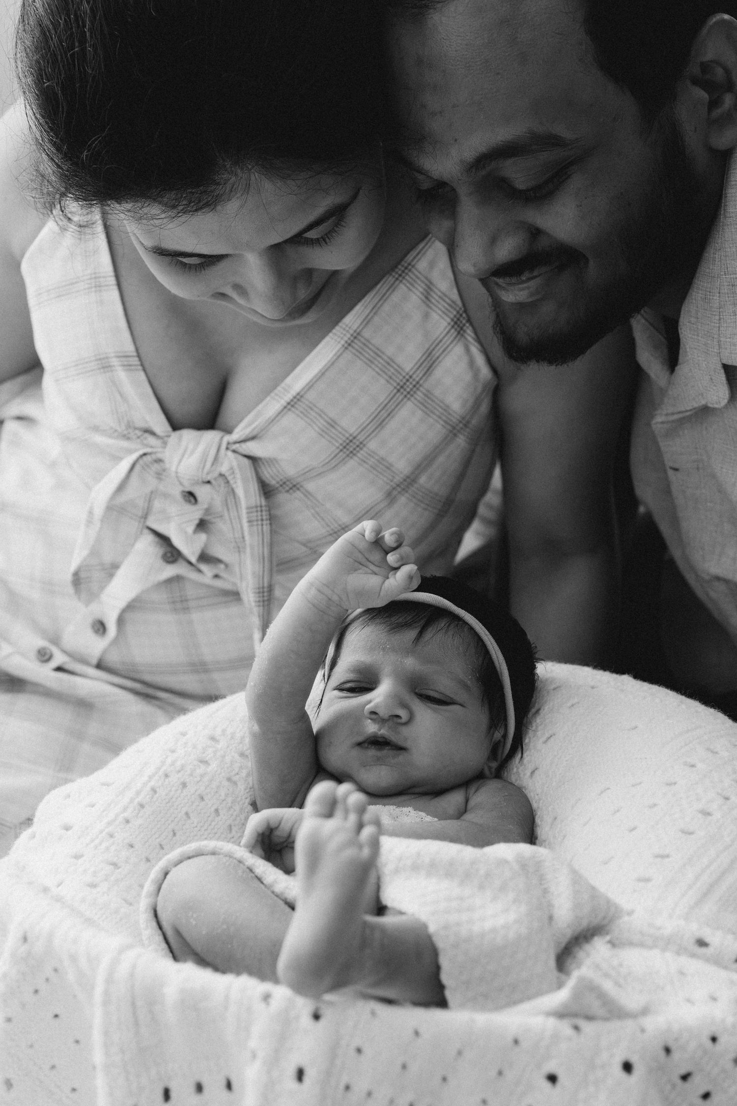 Black and white photo of parents lovingly gazing at their newborn baby wrapped in a white blanket.