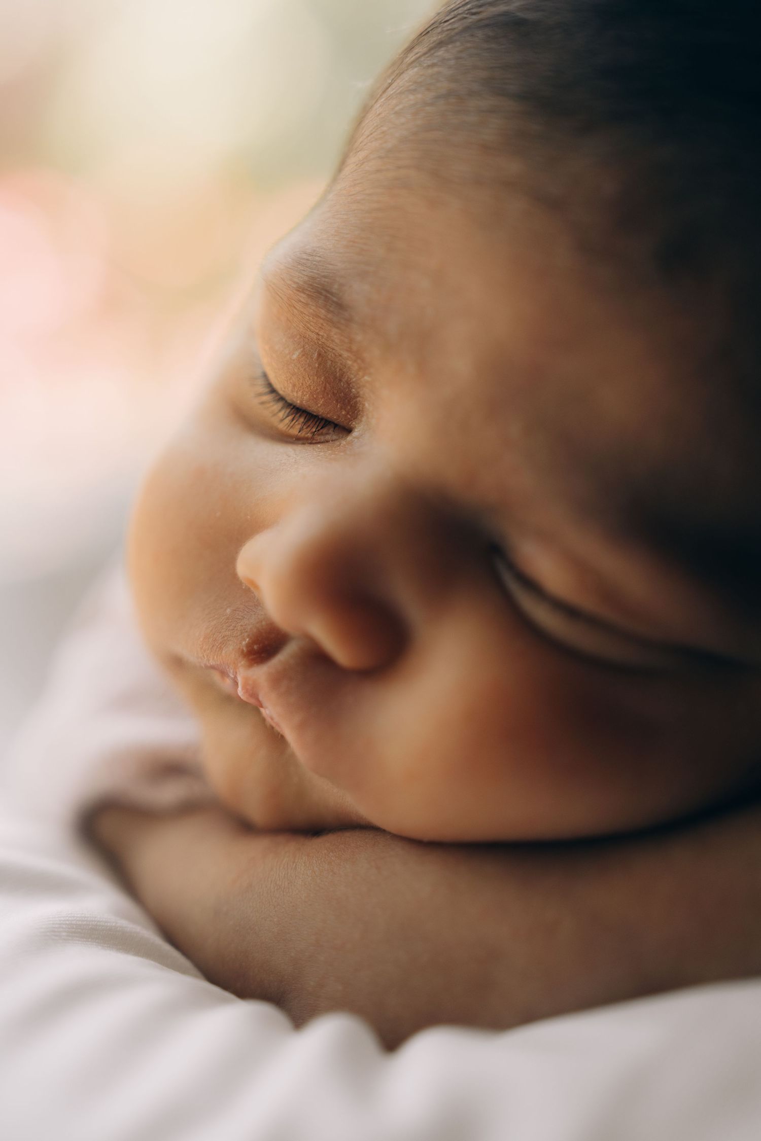 Close-up of a peaceful sleeping newborn baby with soft skin resting their head on tiny hands.