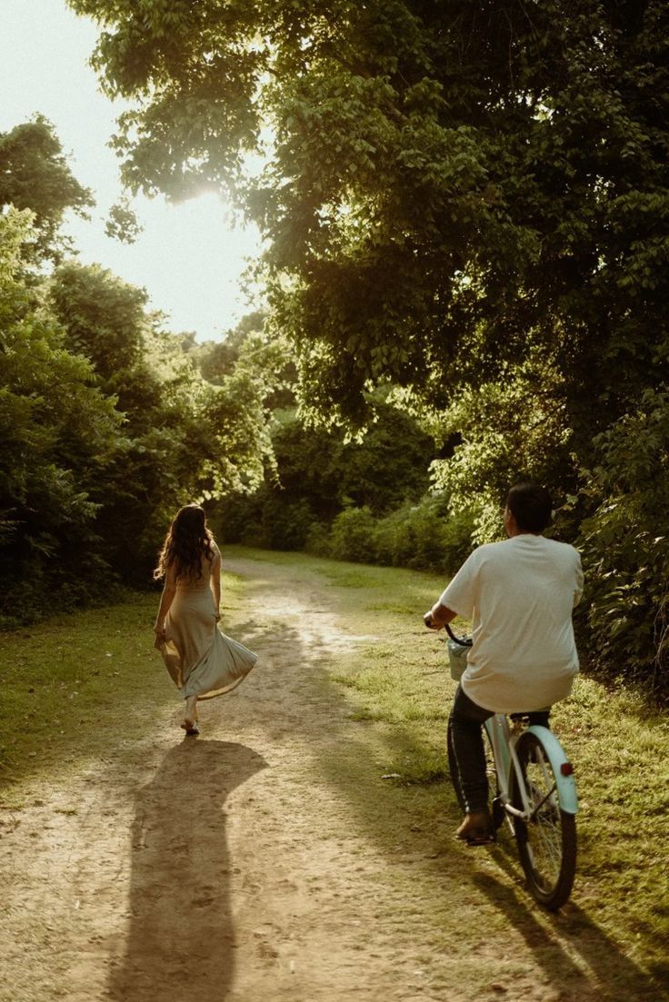Couple riding bikes together on a sunlit dirt path through lush greenery.